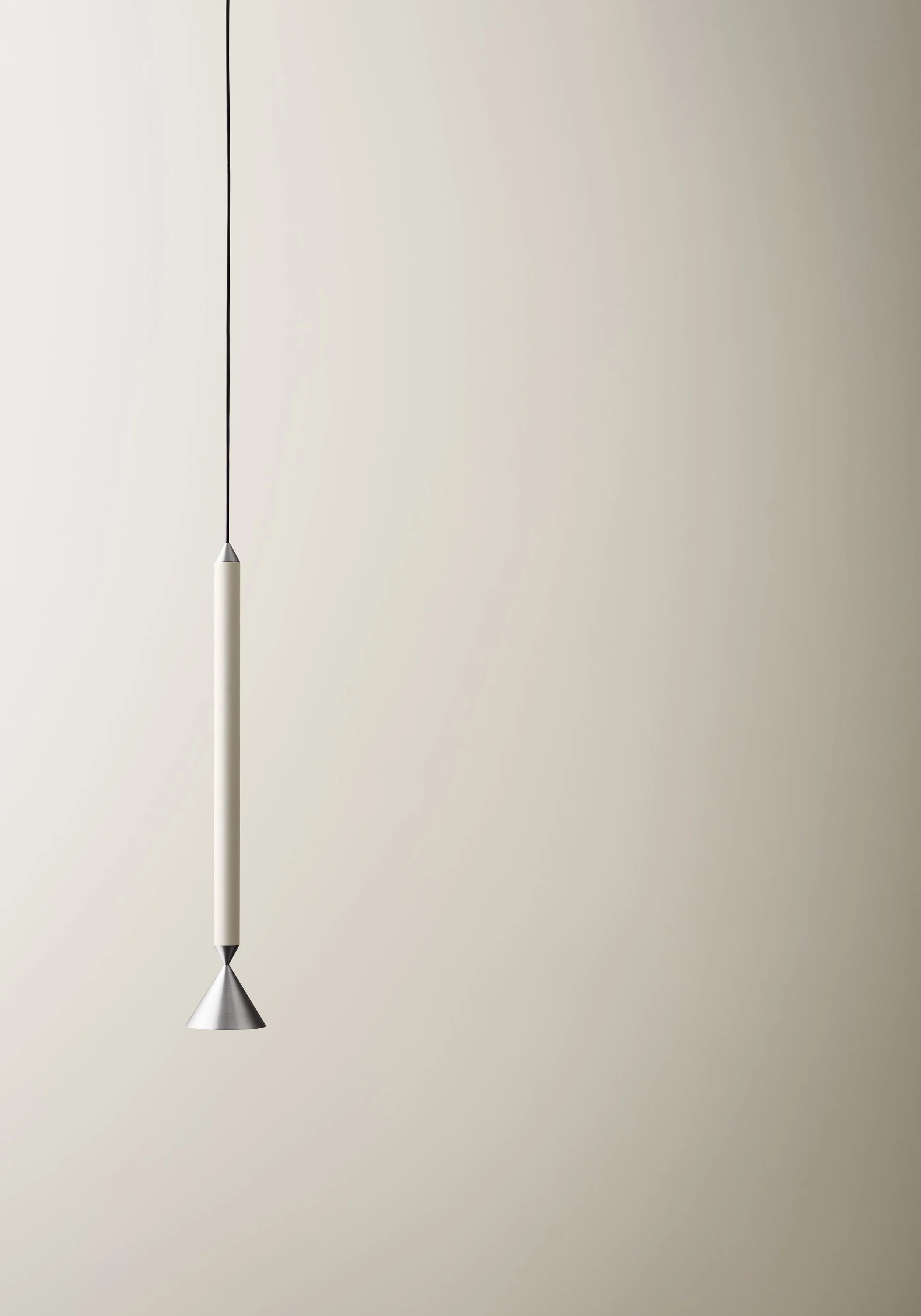A modern, minimalist hanging pendant light with a sleek, tubular design and metallic conical ends, hanging against a plain light-colored wall.