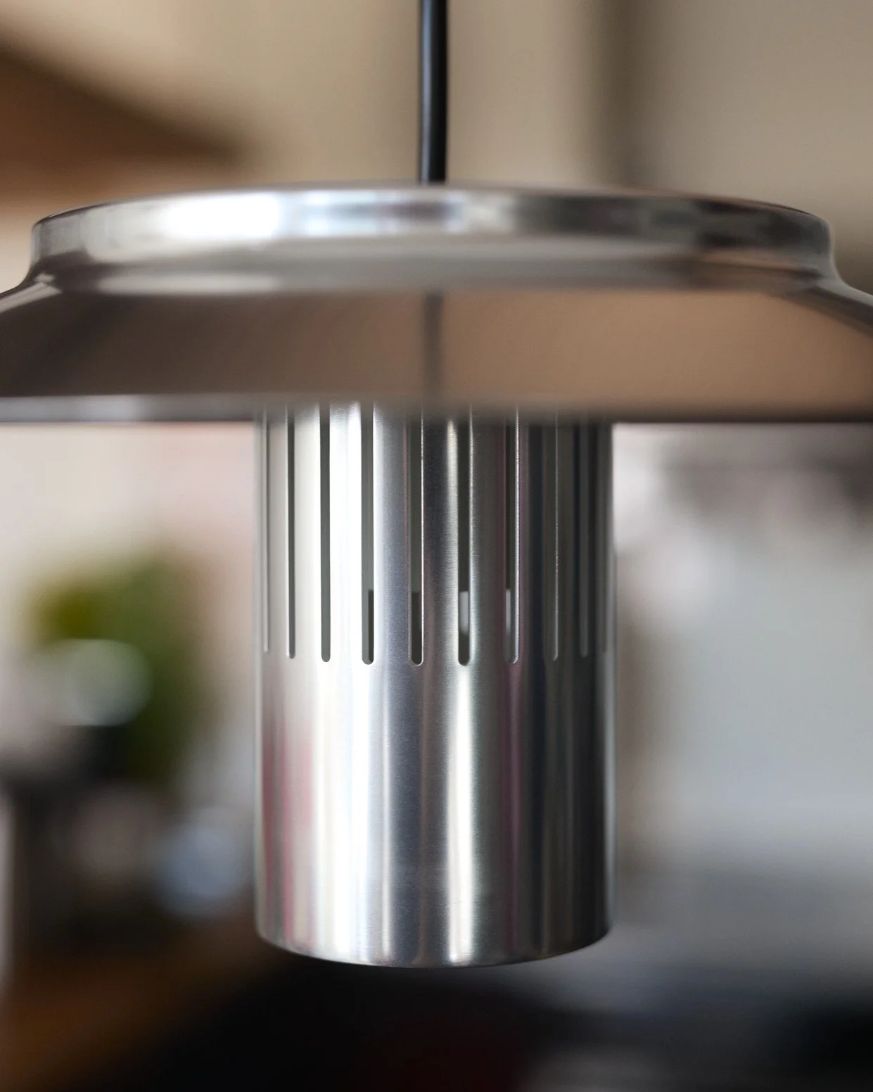 Close-up of a metallic hanging lamp with a cylindrical base and elongated vertical slits, with the ceiling visible behind.