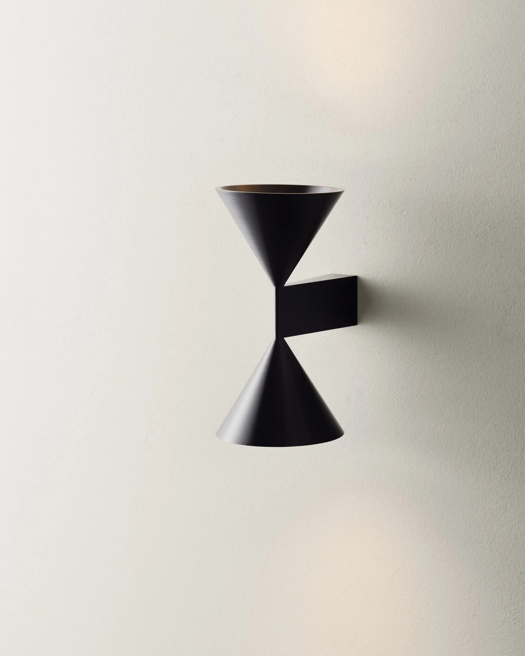 Black modern wall sconce with conical shades on a light-colored wall.