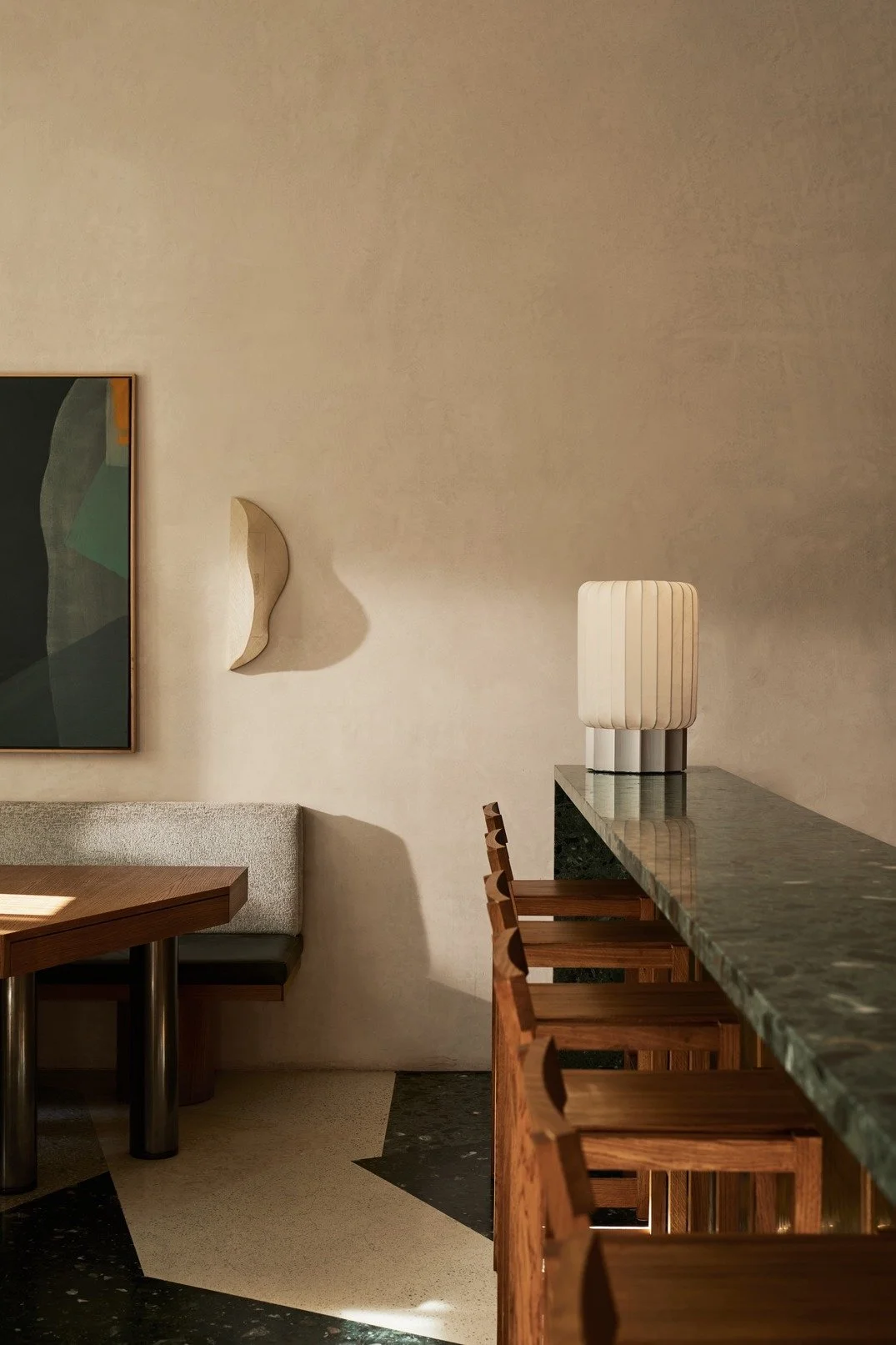 Interior of a modern room with a bar counter, wooden chairs, a lamp, wall art, and decorative wall hook.