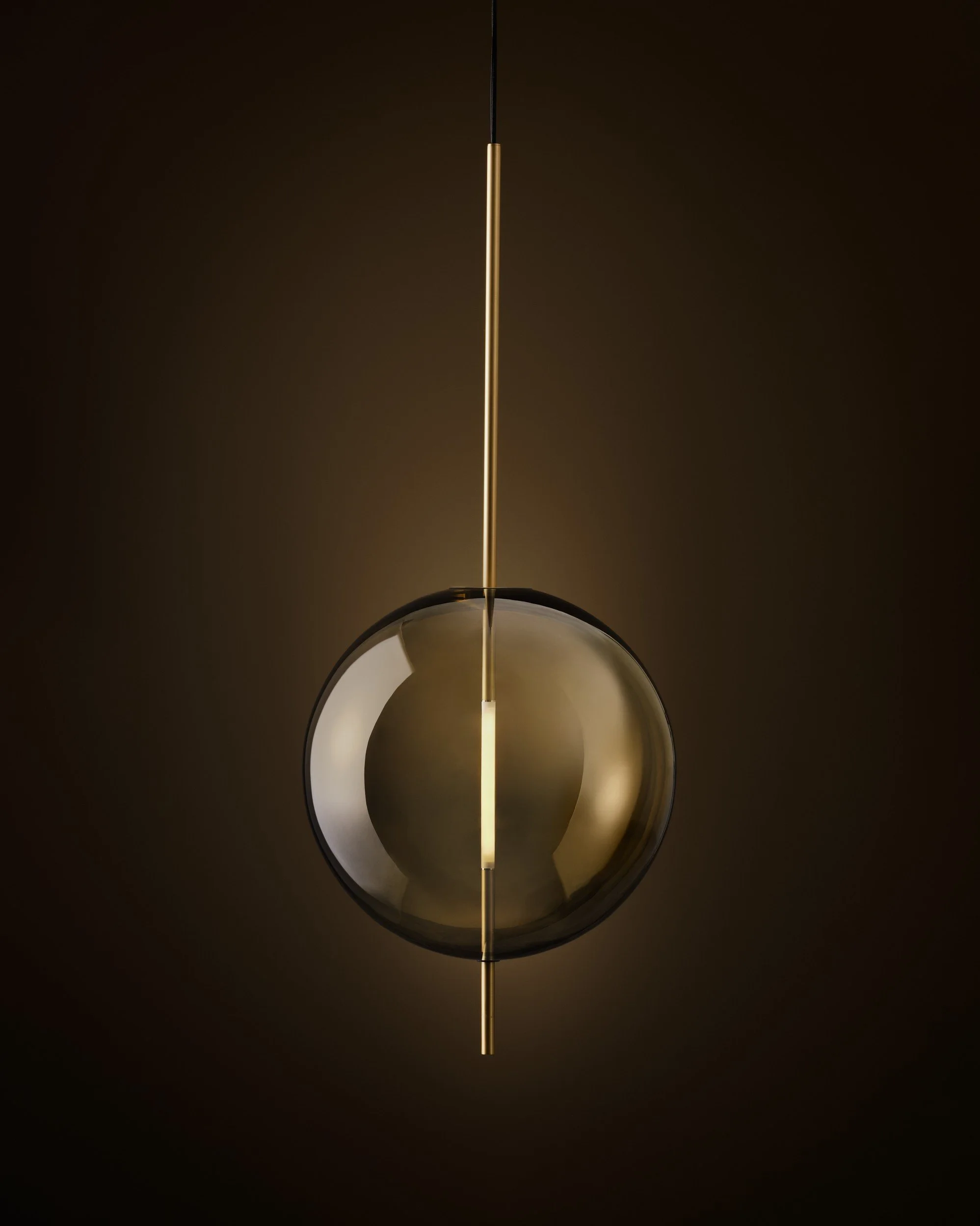 Modern pendant light fixture with a spherical glass shade and a vertical gold rod in the center, hanging against a dark background.
