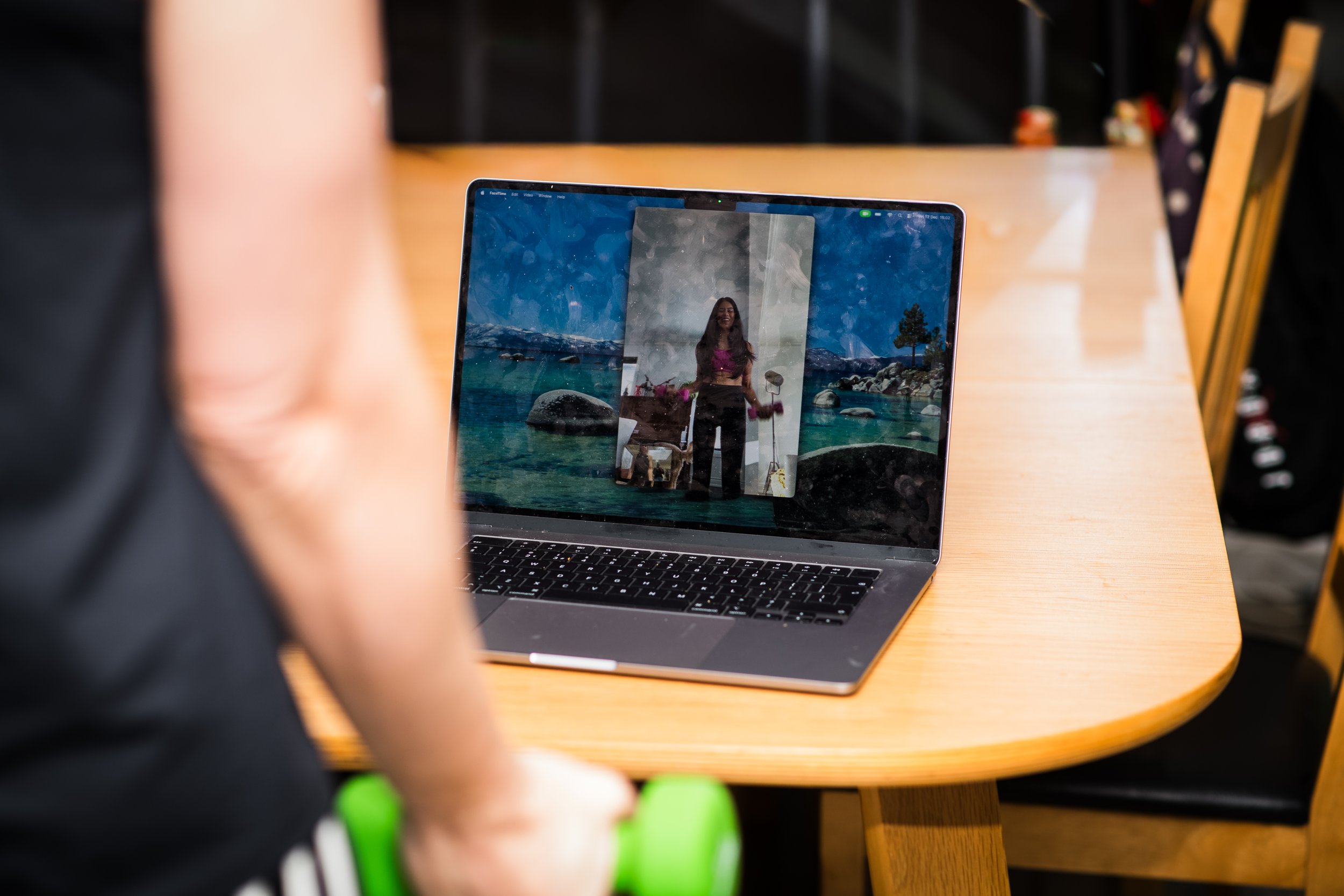 A person is taking a photo of themselves on a laptop screen showing a woman in front of a scenic landscape of mountains, lake, and rocks.