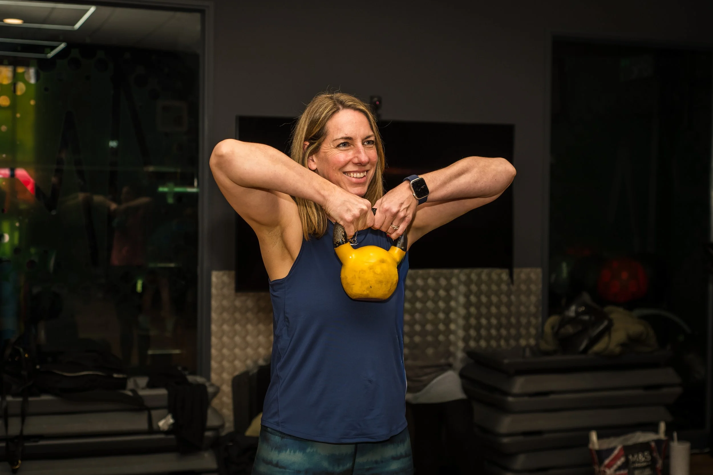 A woman in athletic clothing lifting a yellow kettlebell in a gym.