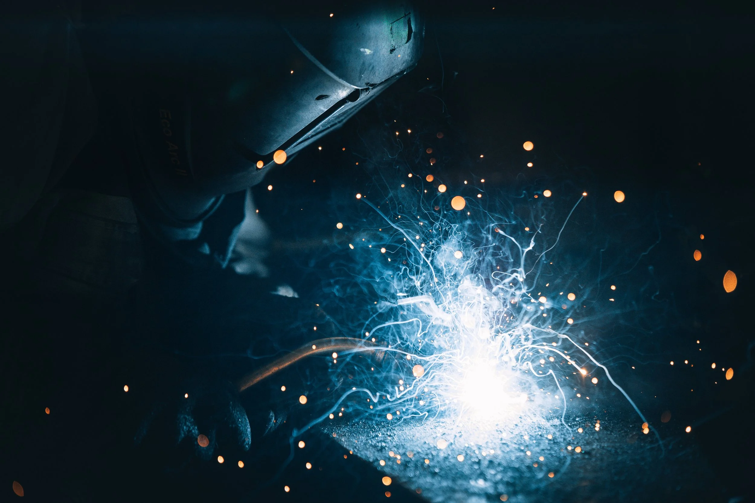 Person welding metal, sparks and bright light emanating from the welding process in a dark environment.
