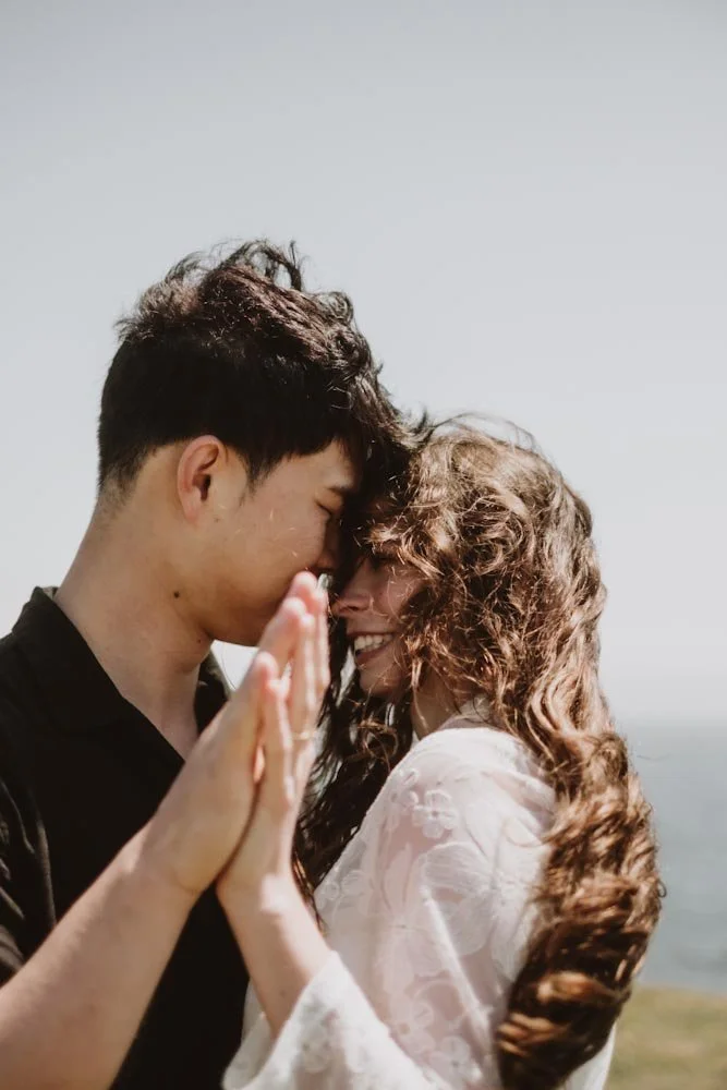 A couple sharing a close, joyful moment outdoors, with their foreheads touching and hands pressed together.