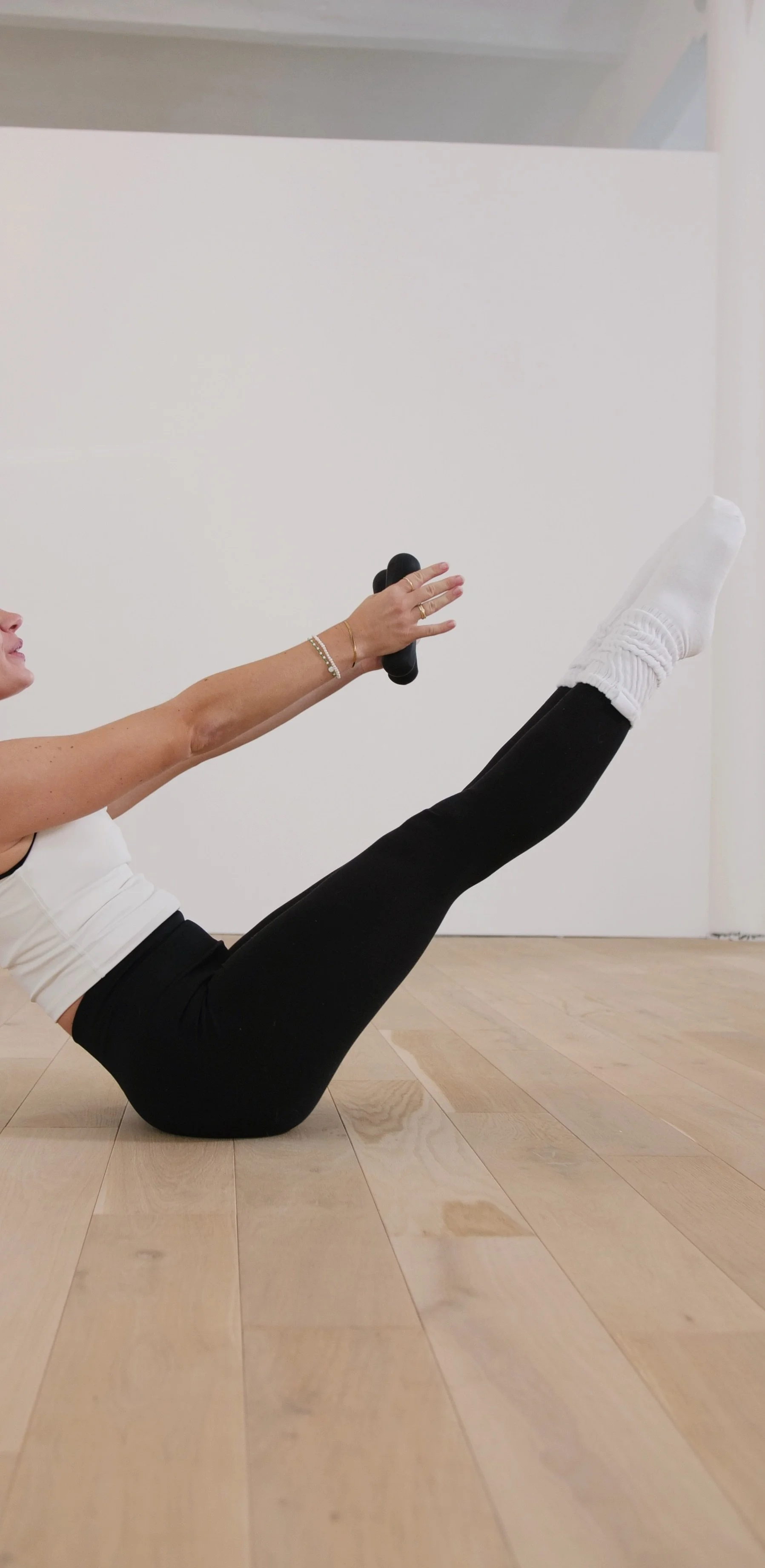 Frau beim Pilates-Workout, die auf dem Boden liegt, ein Bein hochhebt und ein Handgewicht hält.