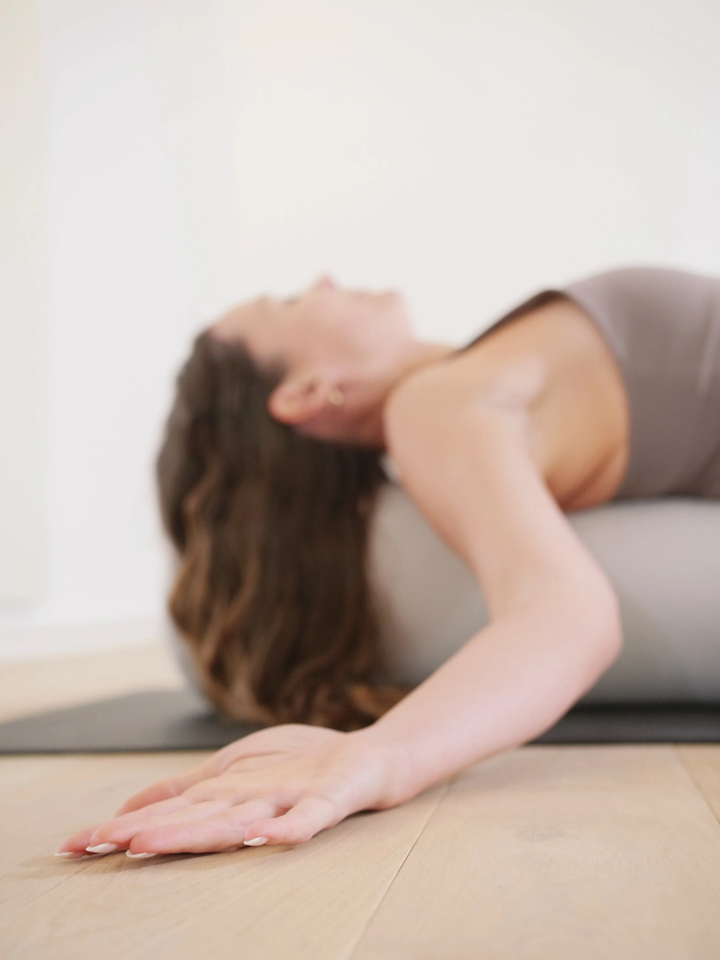 Eine Person liegt auf dem Boden und streckt den Rücken. Die Haare sind braun, die Haut ist hell. Es wird eine Yoga- oder Meditationshaltung eingenommen.