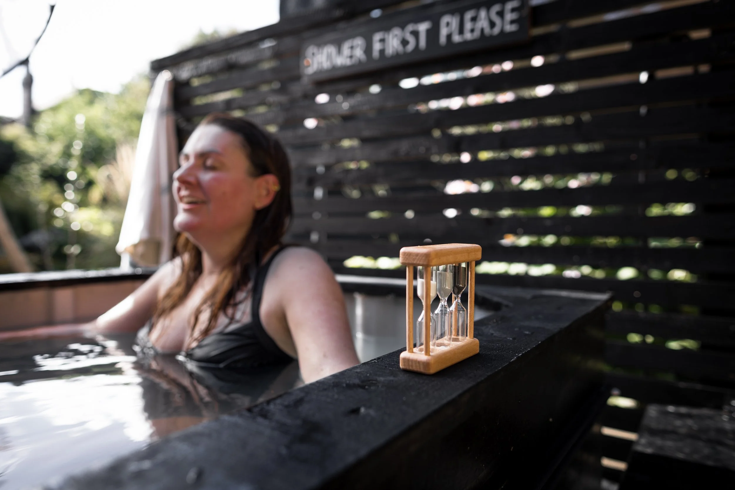 Woman in cold plunge with sand timer. She is smiling!