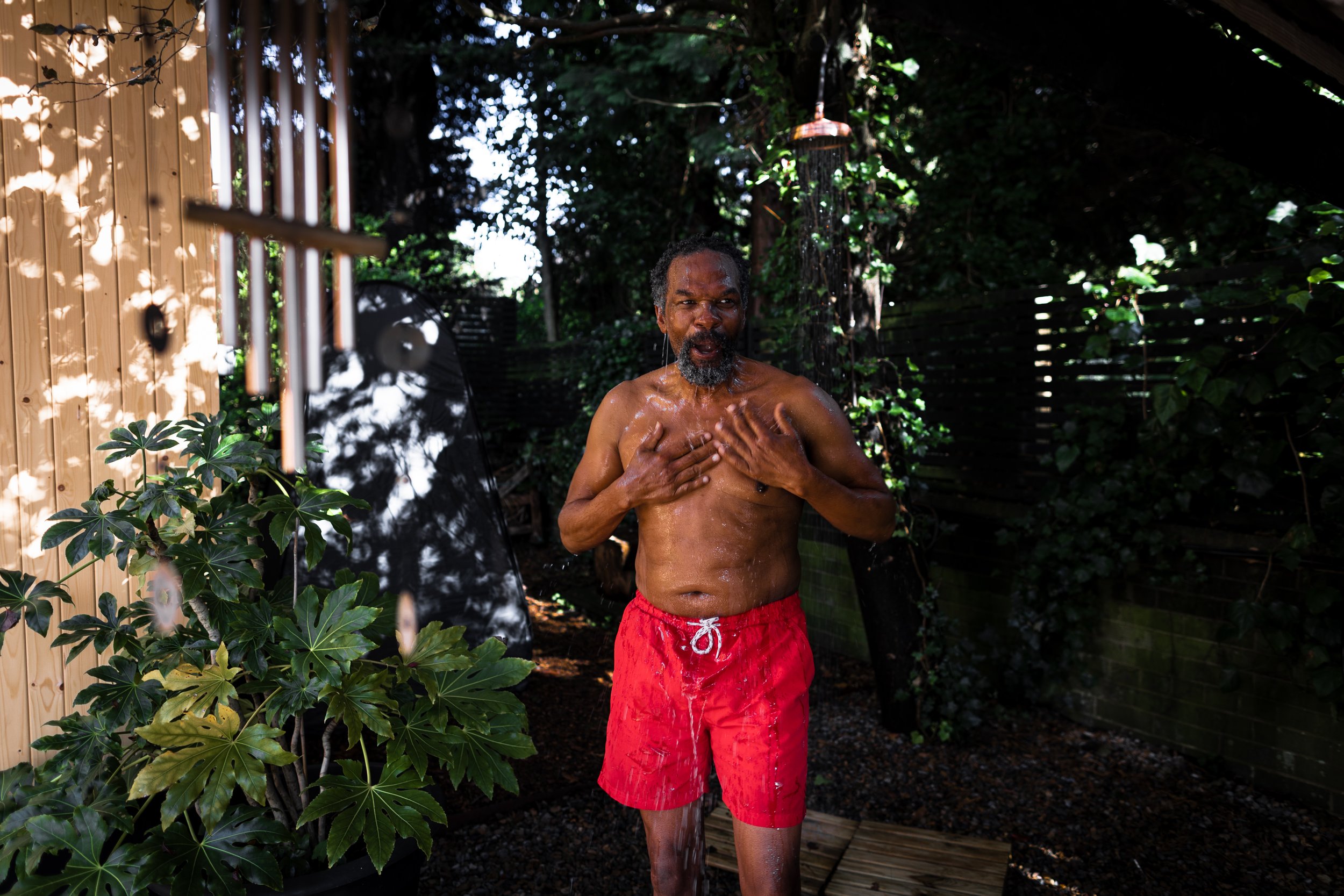 Man in red shorts smiling  under cold shower