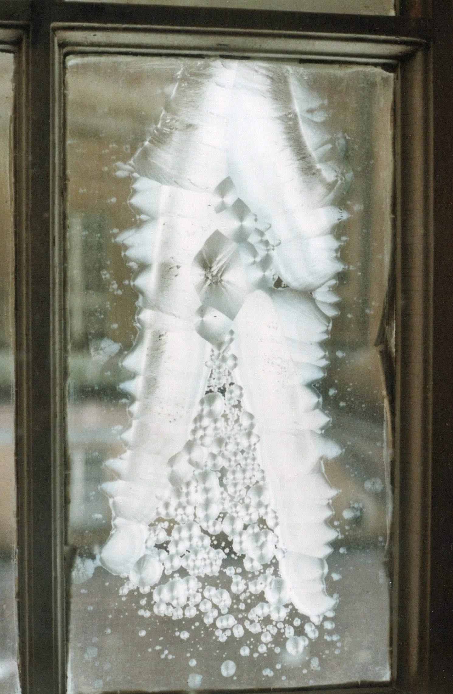 Vergittertes Fenster mit Frostmustern, die wie eine Schneeflocken-Form aussehen.