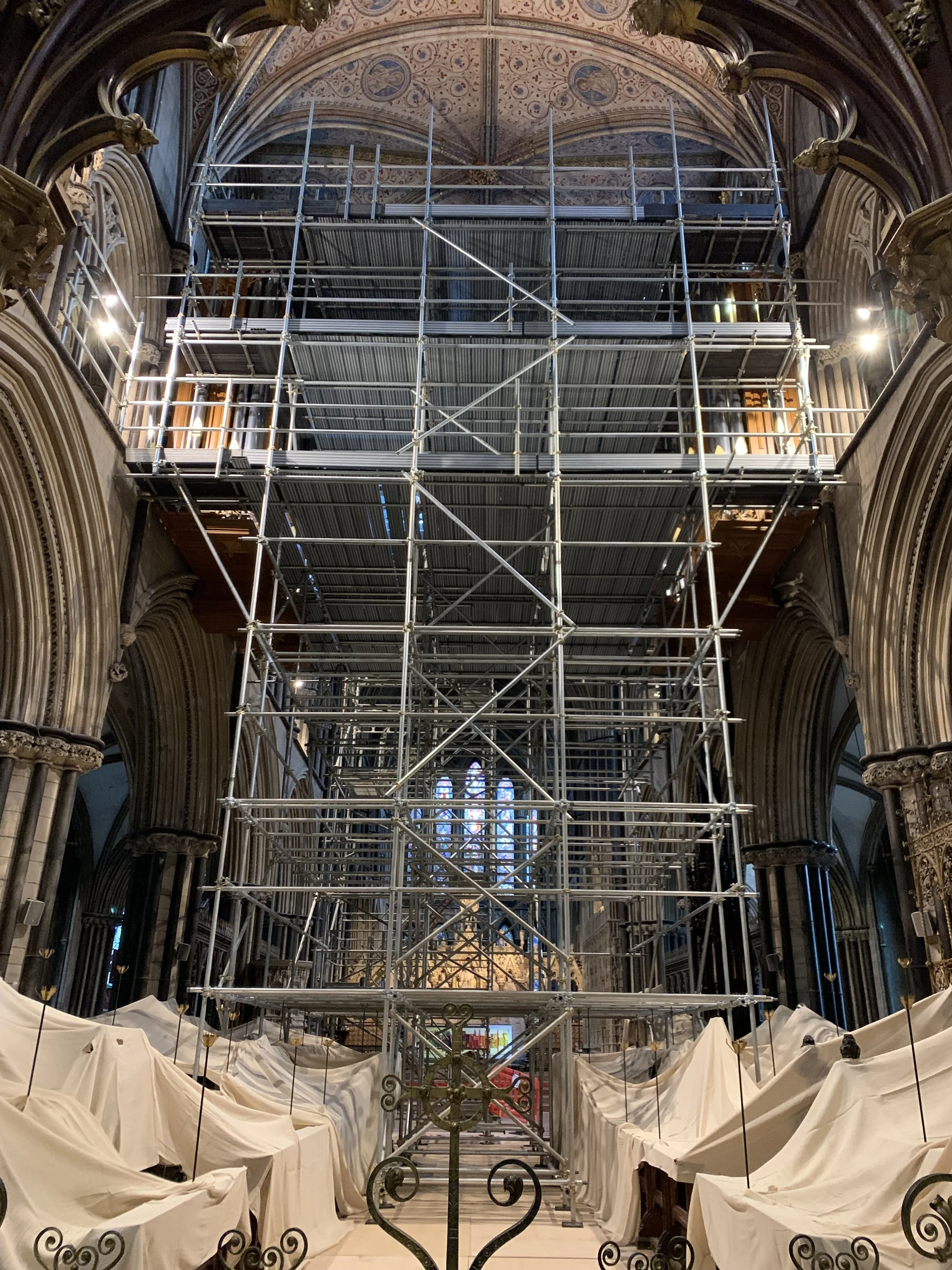 Scaffolding set up inside a large, ornate Gothic cathedral with stained glass windows and detailed architectural features.