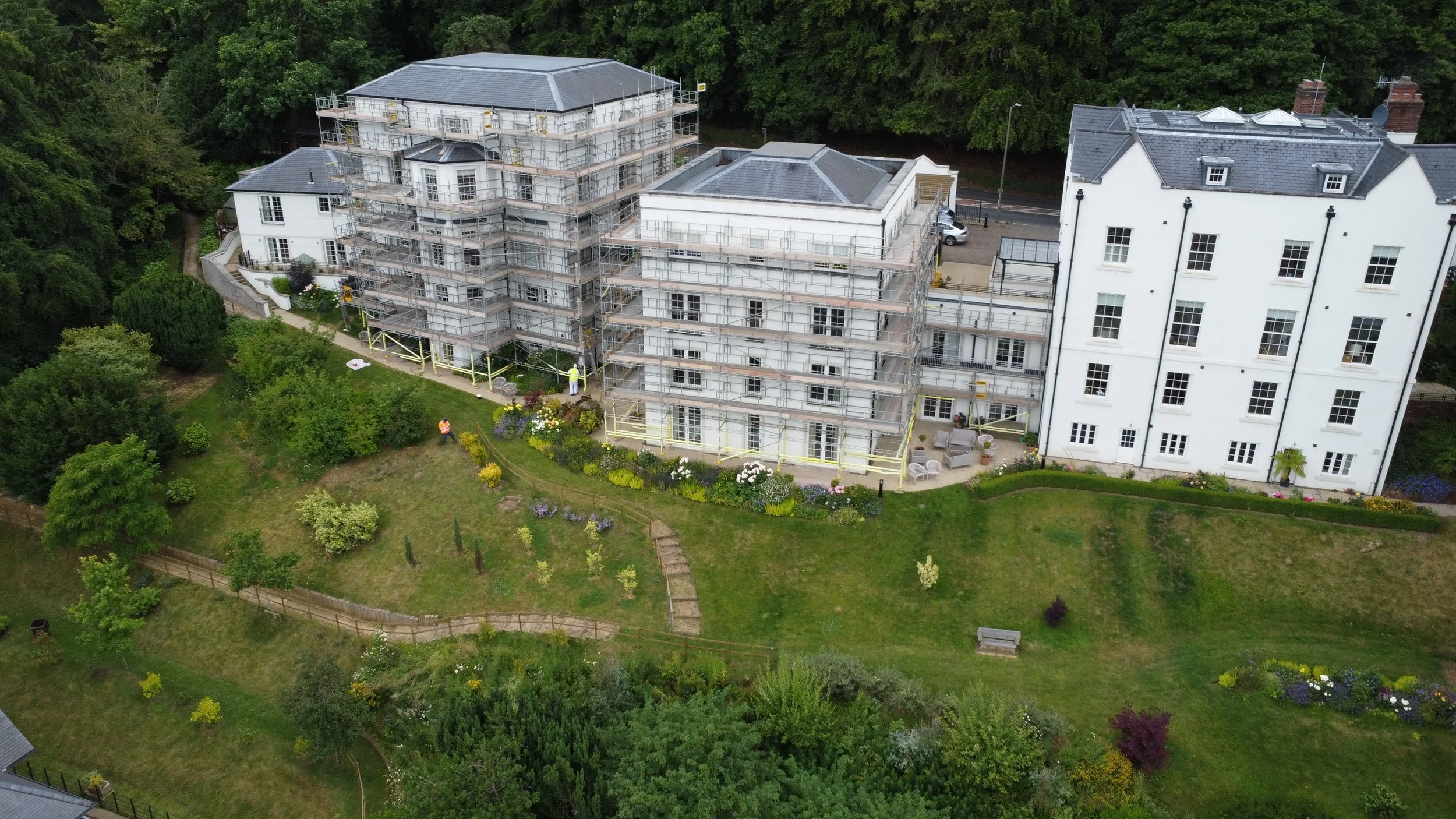 Aerial view of buildings surrounded by trees and greenery, one under construction with scaffolding.