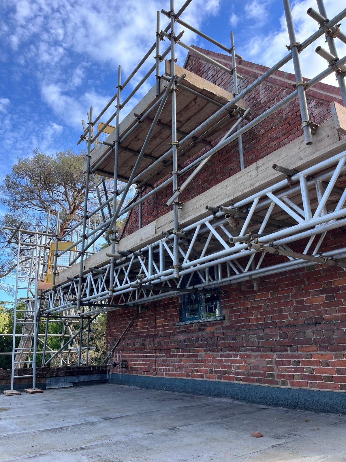 Building facade with scaffolding and brick wall under blue sky with clouds.