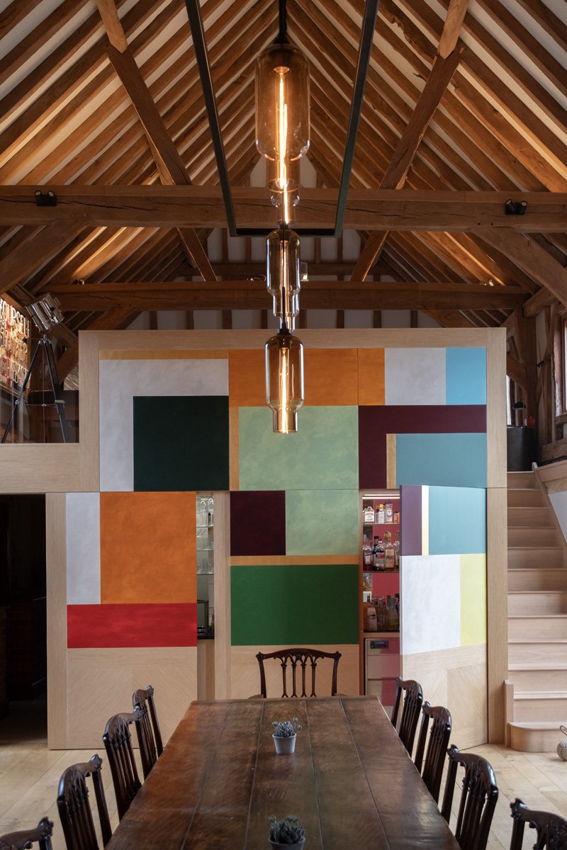 Modern barn convertion interior with vibrant colour block mural on panels doors concealing a drinks cabinet
