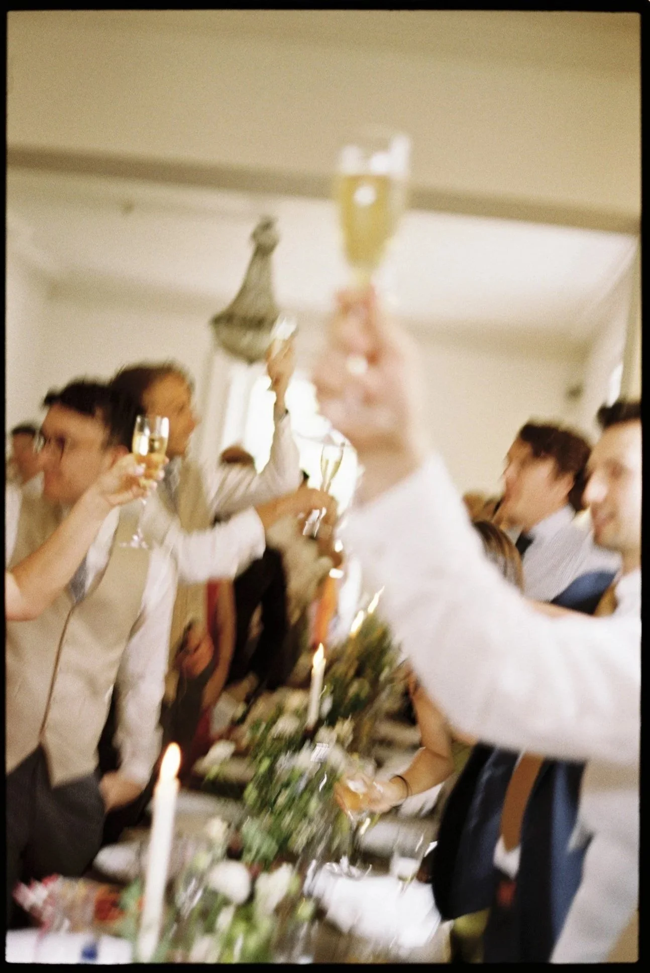 People celebrating at a party, raising glasses of champagne in a toast, in a room decorated with candles and flowers on the table.