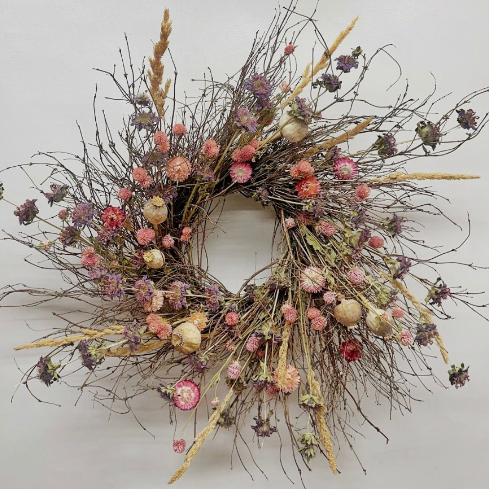 A dried flower wreath with various small, colorful flowers and twigs arranged in a circular shape.