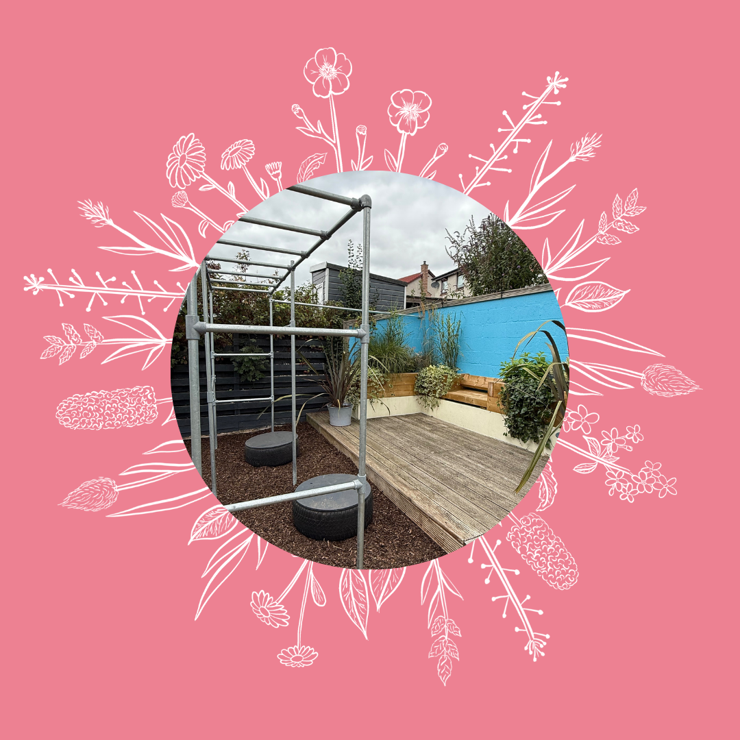 A small outdoor patio with wooden decking, potted plants, and a blue painted wall. There's a metal structure with two tires used as swings or seats, set against a cloudy sky.