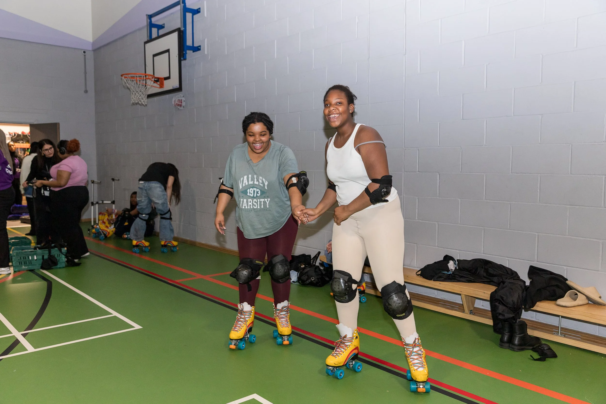 Two young women in sportswear rollerblade at WEST Youth Zone in a basketball court