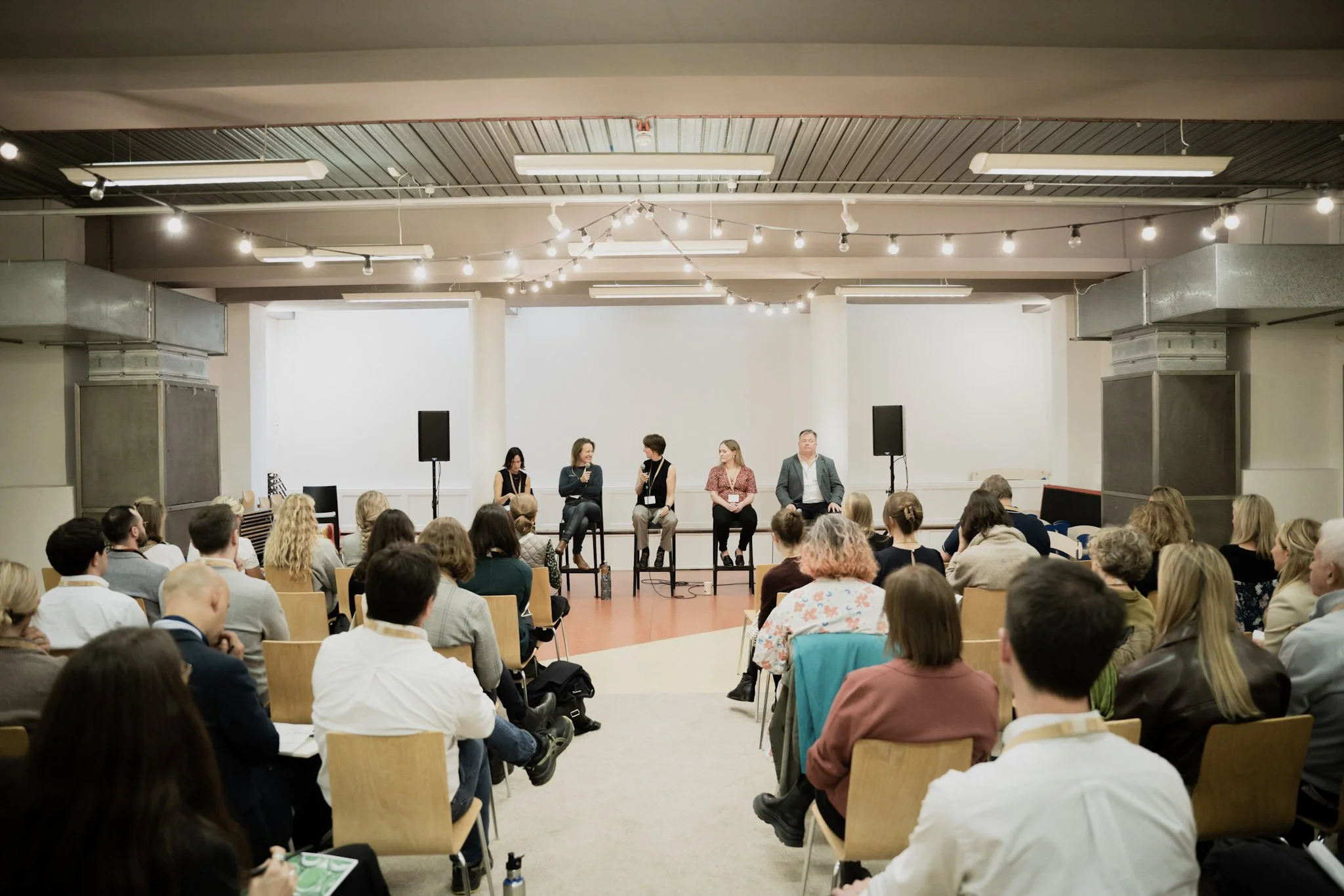 Panel discussion at a conference with five speakers seated on a stage and an audience listening attentively.