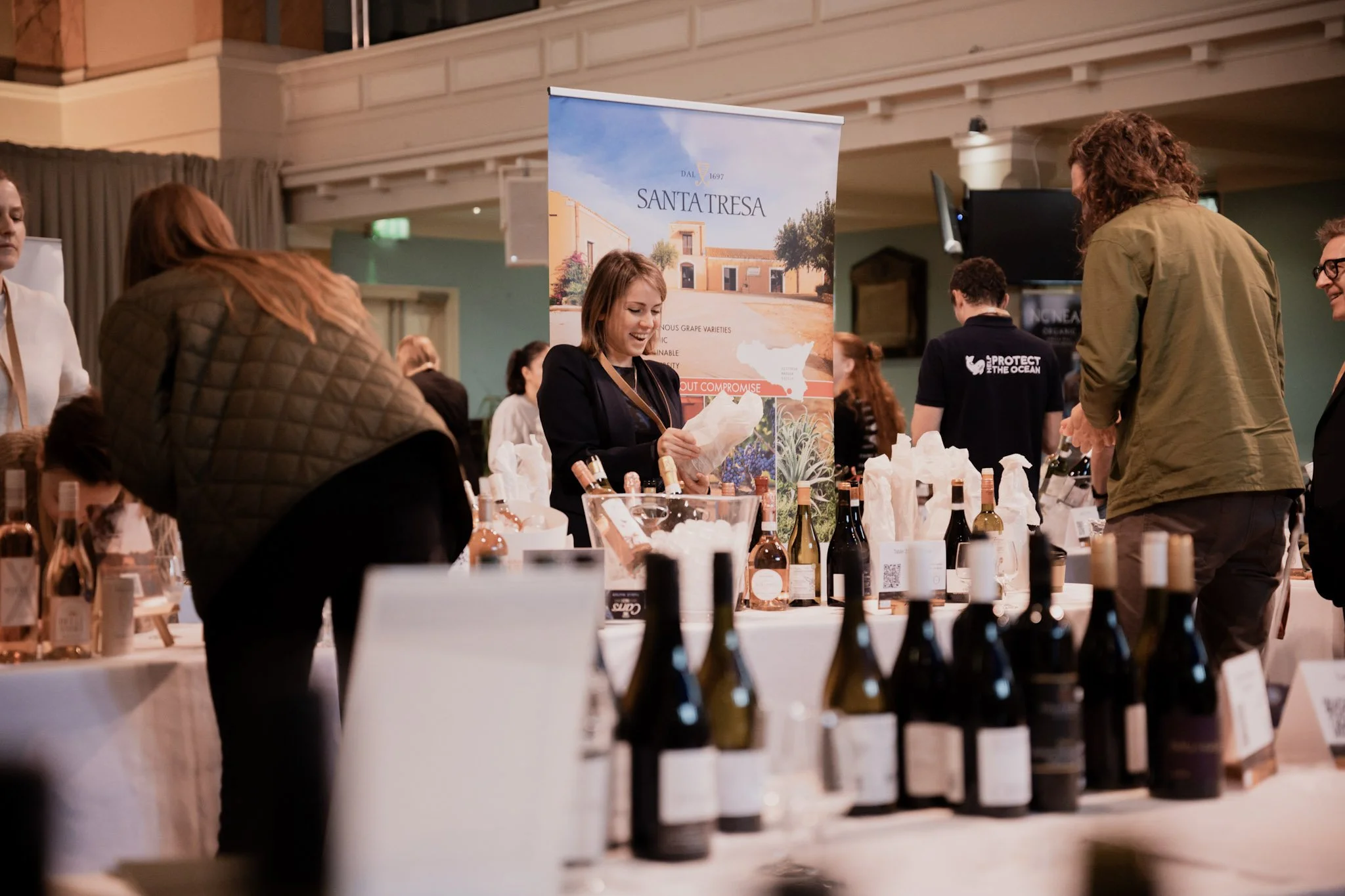 People browsing wine bottles at a wine tasting event with a Santa Teresa banner in the background.