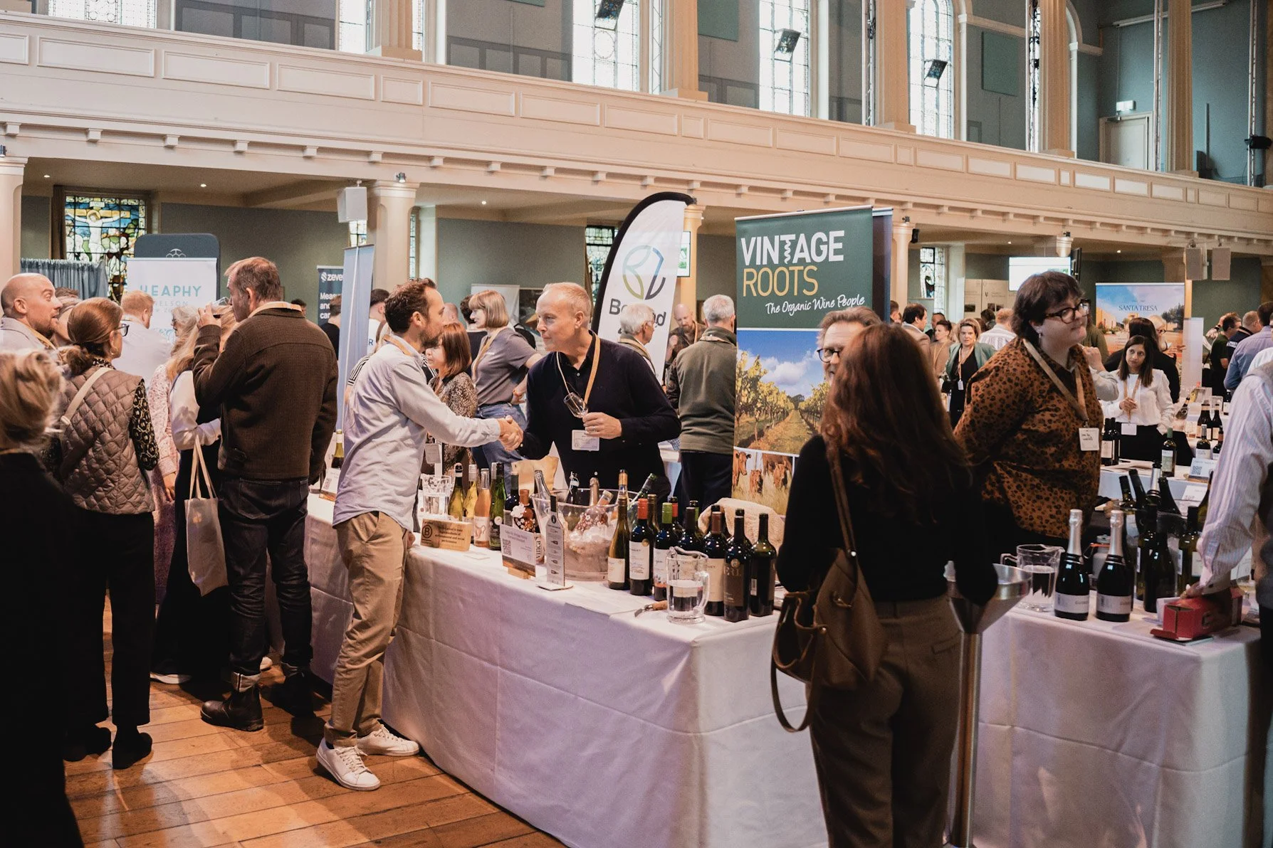 People attending a wine tasting event with various wine bottles on display and banners in an elegant, well-lit hall.