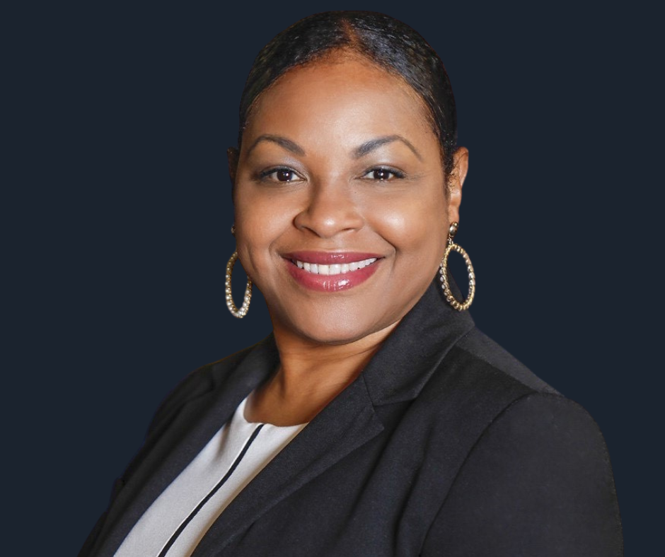 A woman with dark hair, wearing hoop earrings, a black blazer, and a white top, smiling against a white background.