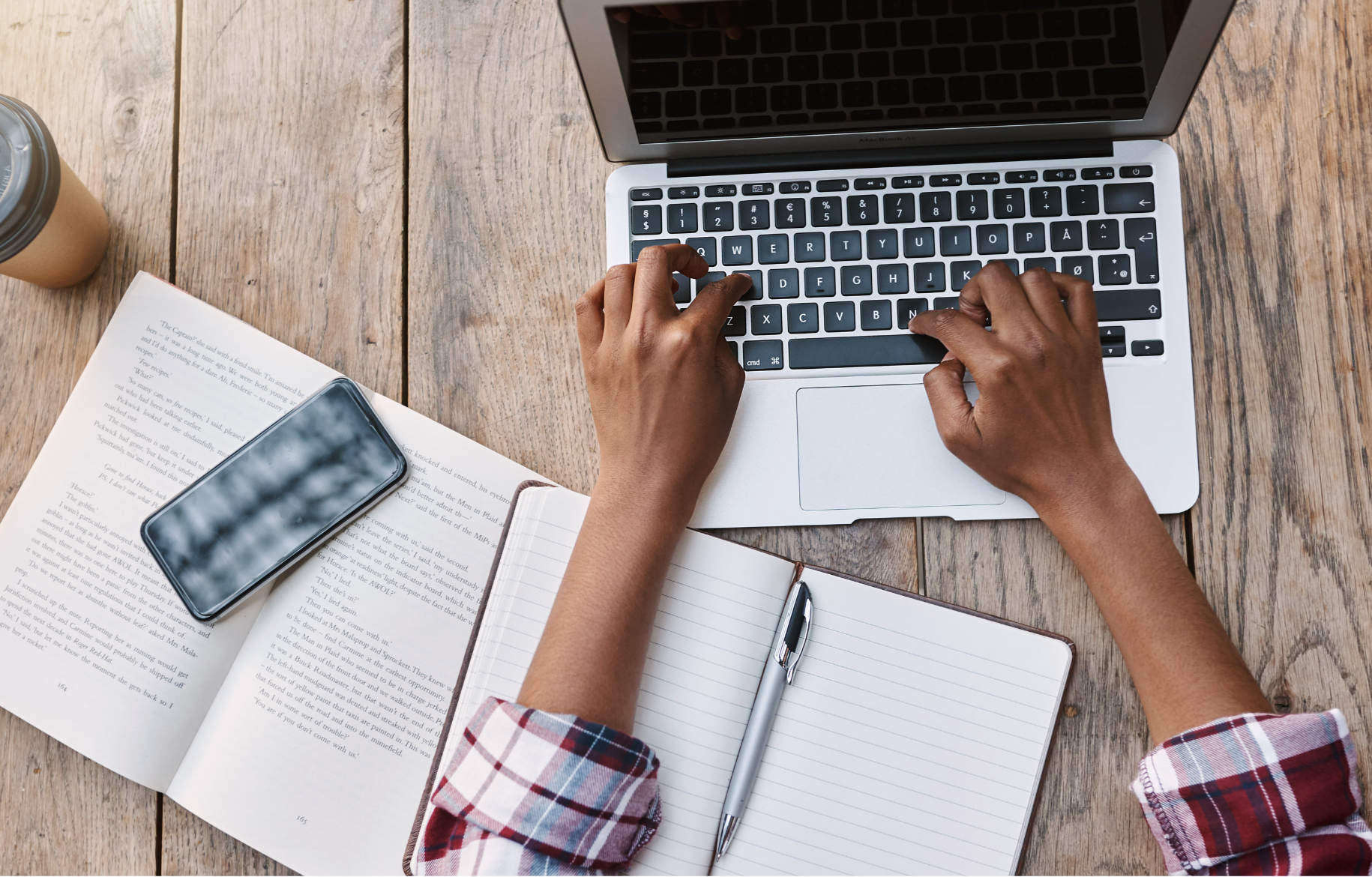 A person's hands on a laptop keyboard with a book and a notebook open nearby.