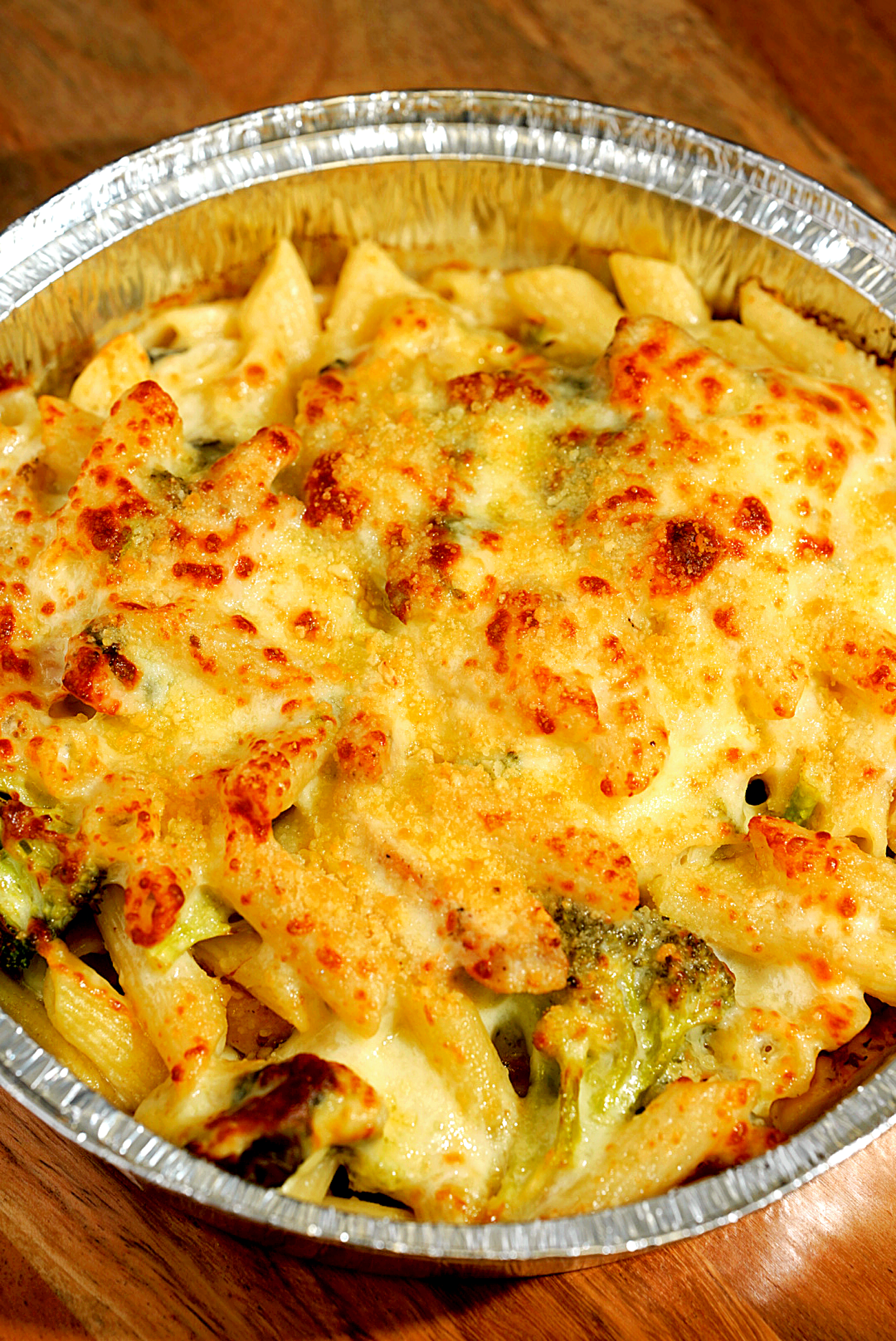 Baked casserole with penne pasta, melted cheese, and broccoli in foil pan