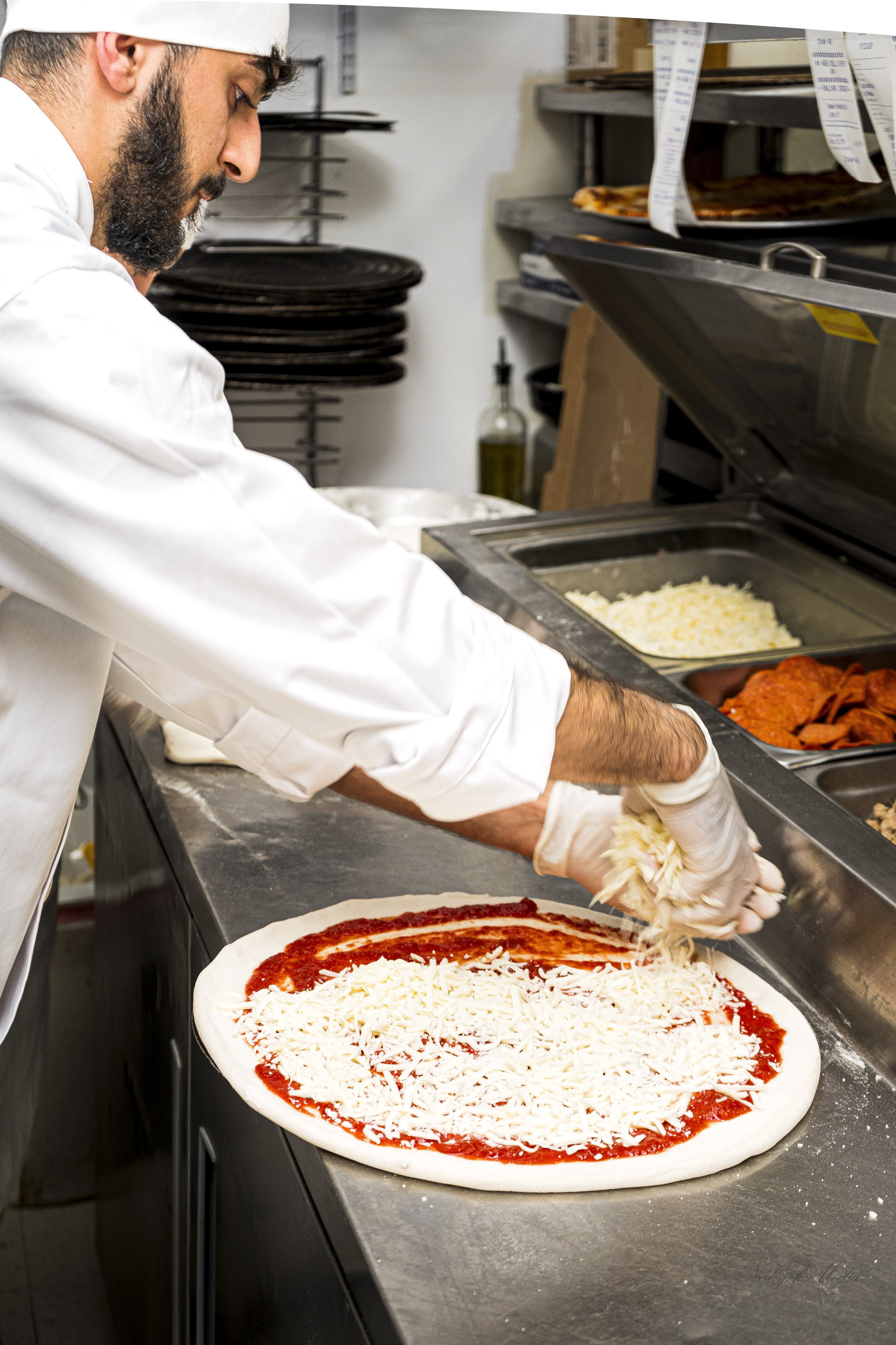 Chef preparing pizza with cheese and tomato sauce in a kitchen.