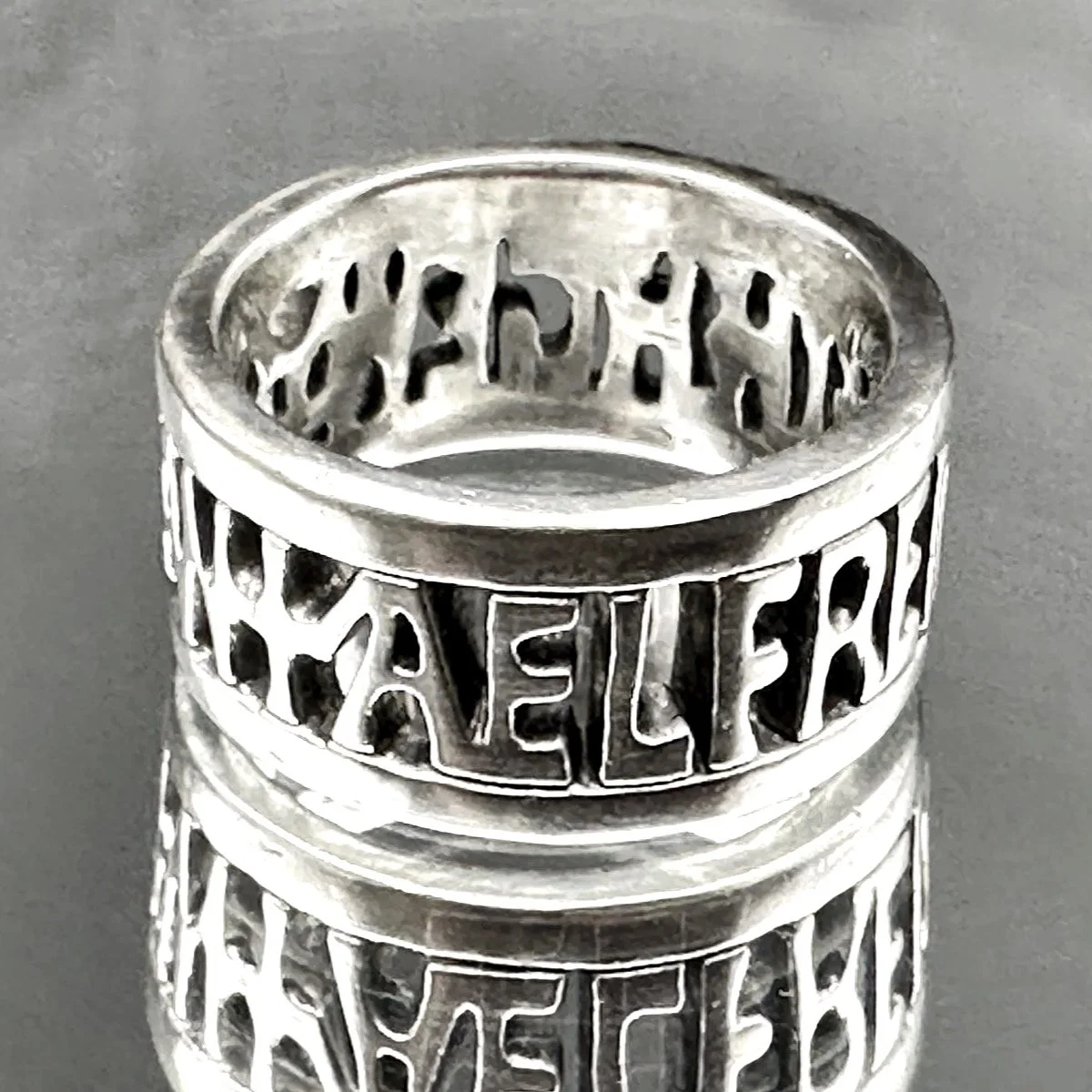 Close-up of The Alfred Ring, handmade in sterling silver, sitting on a mirror