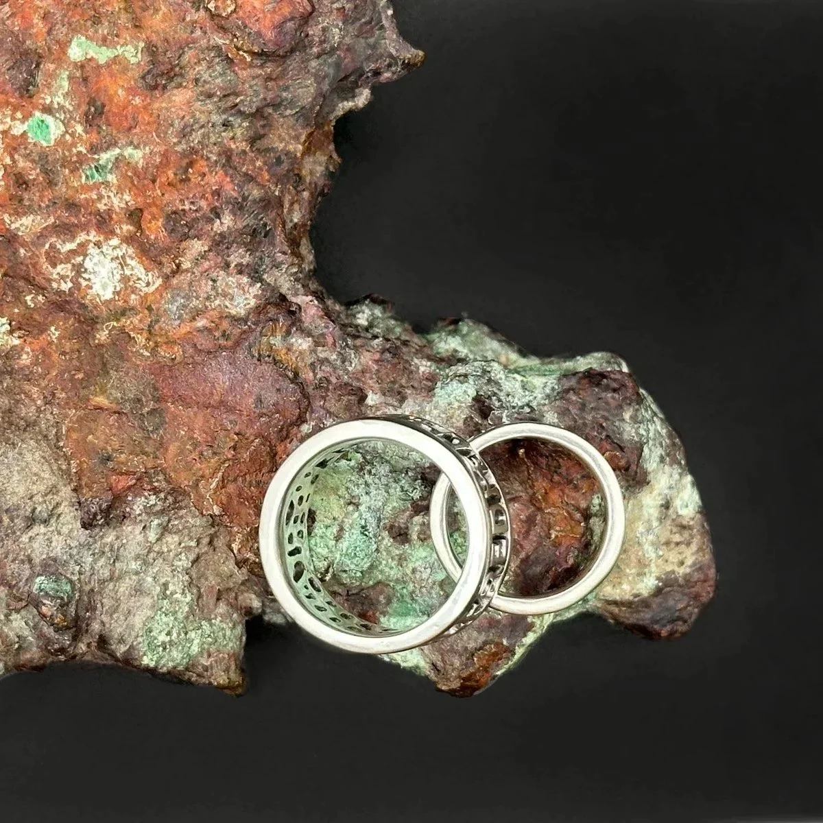 Two hand-forged sterling silver rings from above, resting on tin ore from Wessex