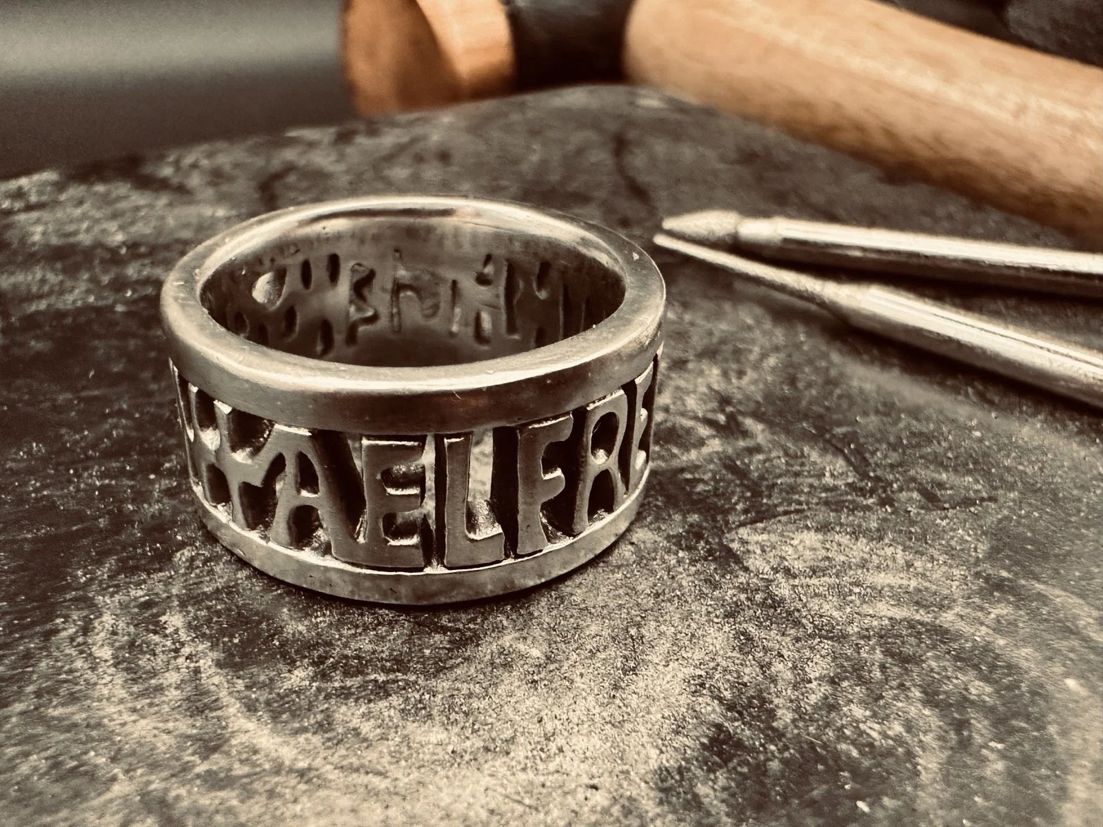 Handmade sterling silver King Alfred the Great ring with the words “Aelfred Mec Heht Gewyrcan”, displayed on a rubber jewellery block with a Thor hammer in the background
