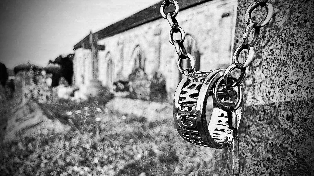 A sterling silver ring inspired by 9th-century Anglo-Saxon and Norse England, hanging on a chain from a gravestone in front of an ancient English church
