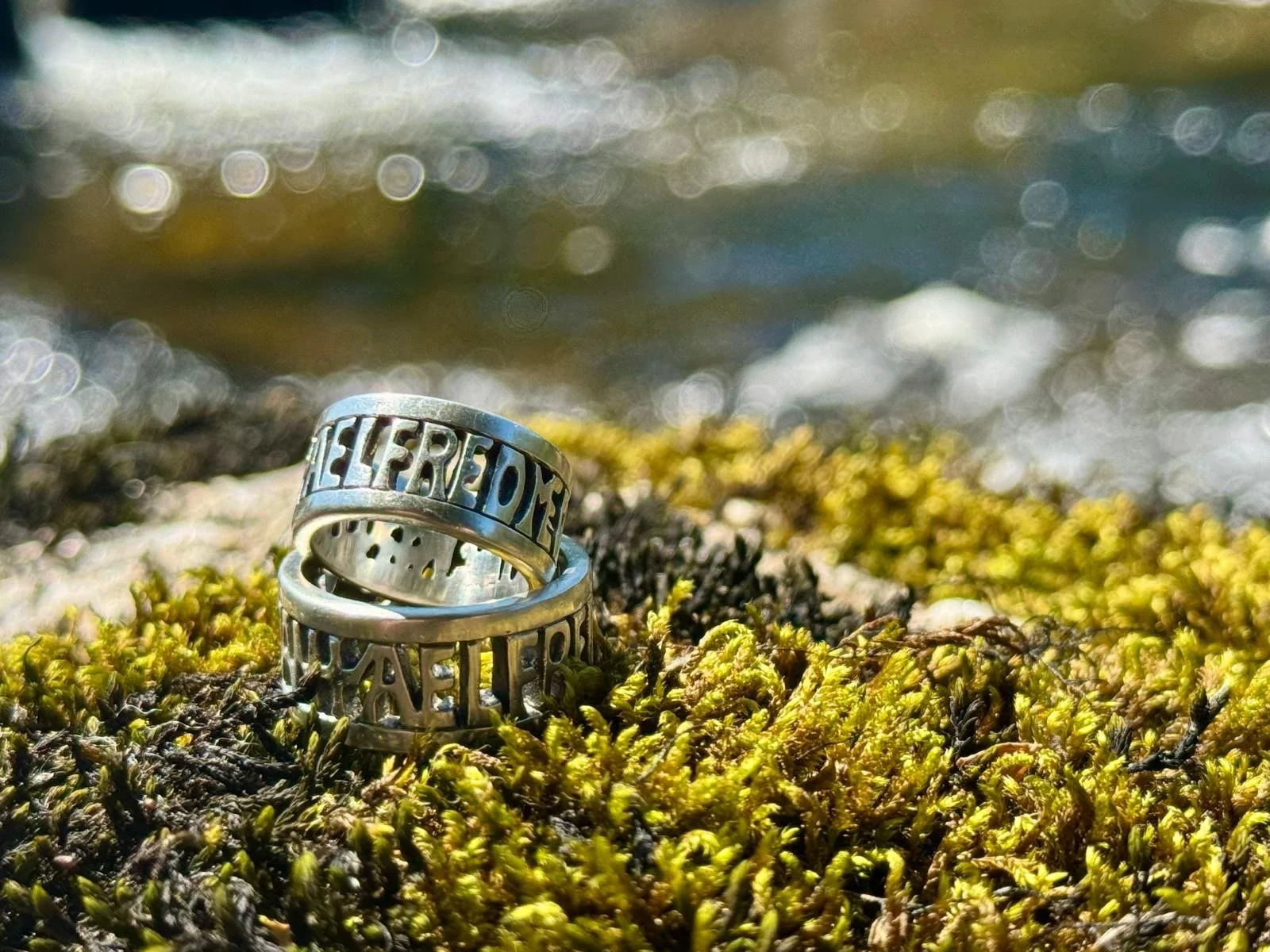 Two Alfred the Great rings inspired by the Alfred jewel, sitting on a moss covered rock with river water flowing behind