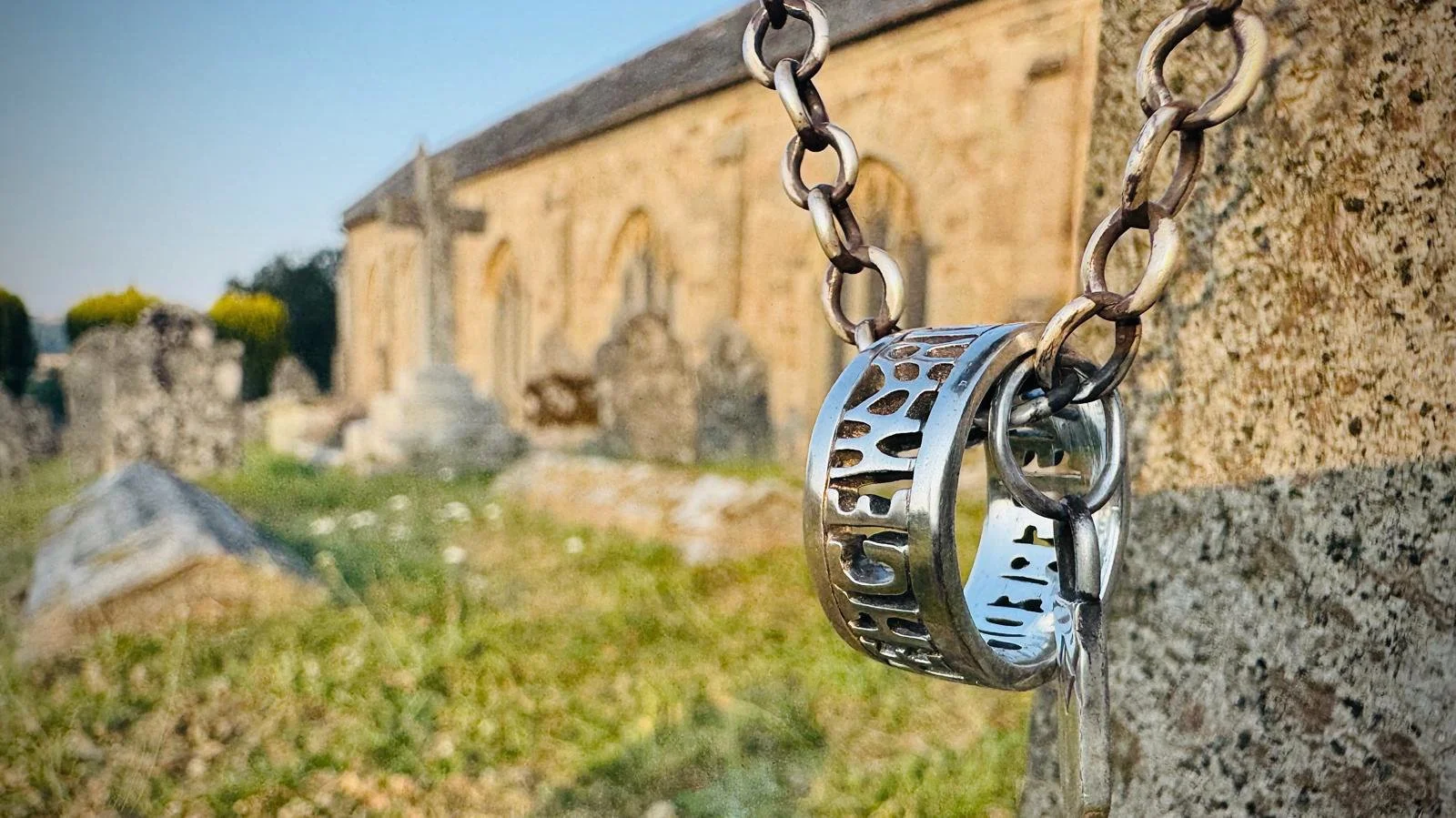 A sterling silver ring inspired by 9th-century Wessex, hanging on a chunky chain from a gravestone in front of an ancient English church