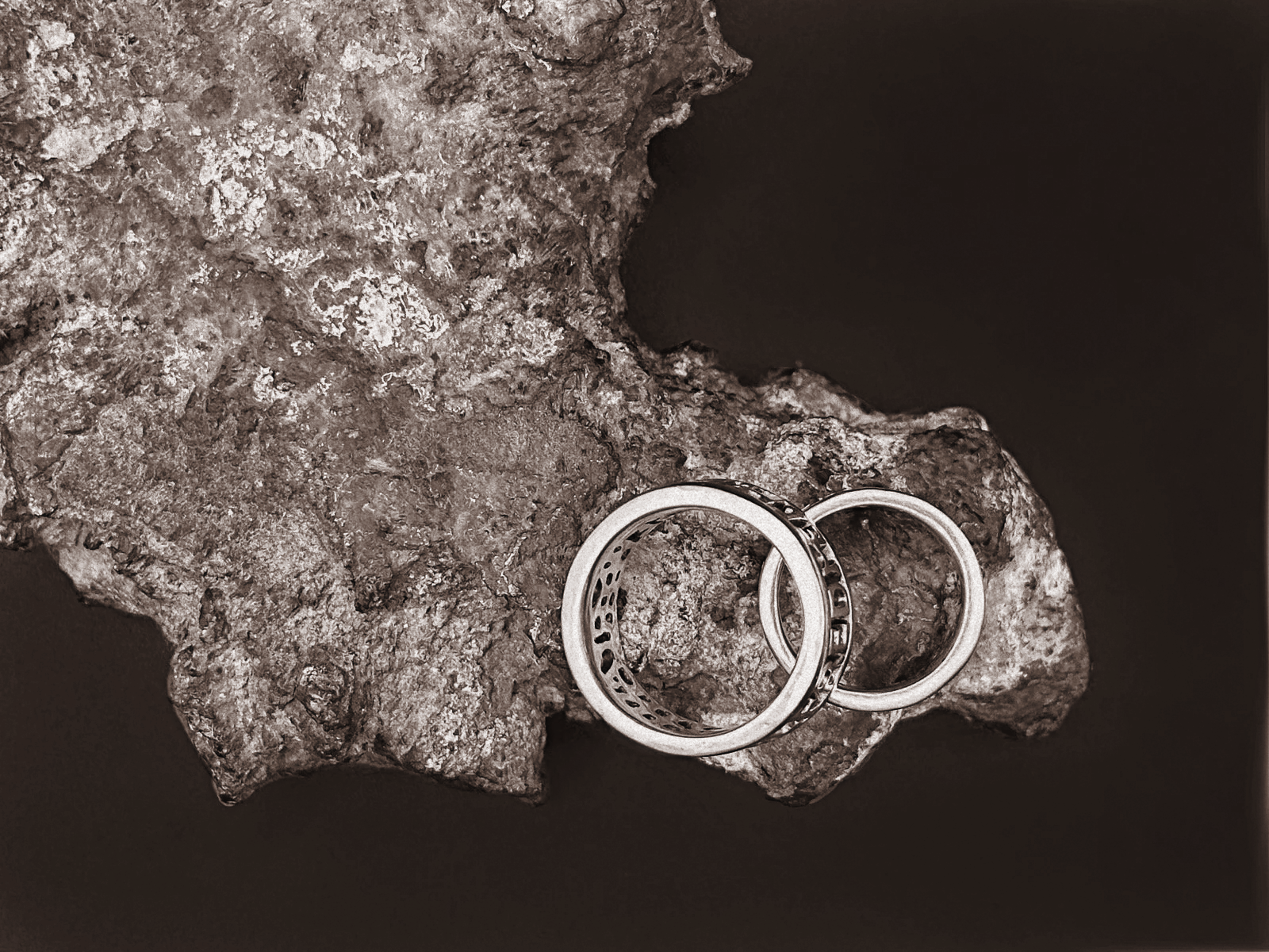 Two hand-forged sterling silver rings from above, resting on tin ore from Wessex