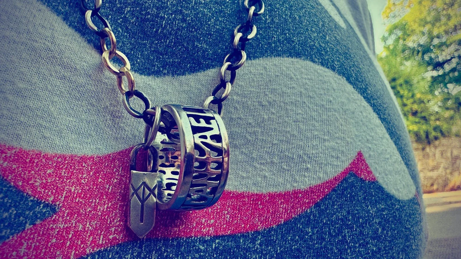 Alfred the Great inspired sterling silver ring hanging from a chain against a man’s chest, with the words “Aelfred Mec Heht Gewyrcan” (Alfred had me made), taken from the Alfred Jewel