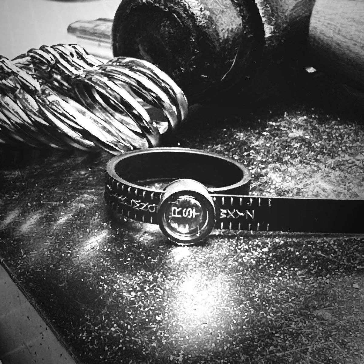 Image of a black plastic ring sizer with magnifier window on black jeweller's block and Thor hammer and ring gauge in the background.