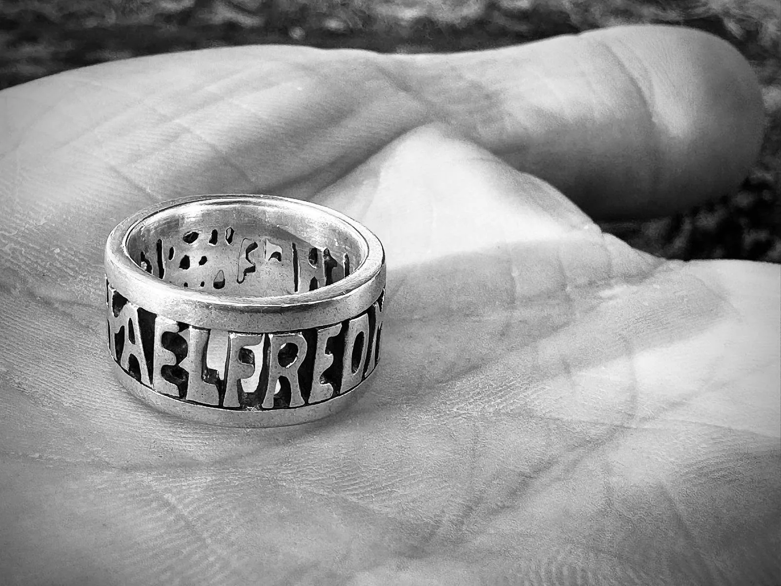 Black and white of an Alfred the Great, Aelfred Mec Heat Gewyrcan, ring resting in the palm of a man’s hand.