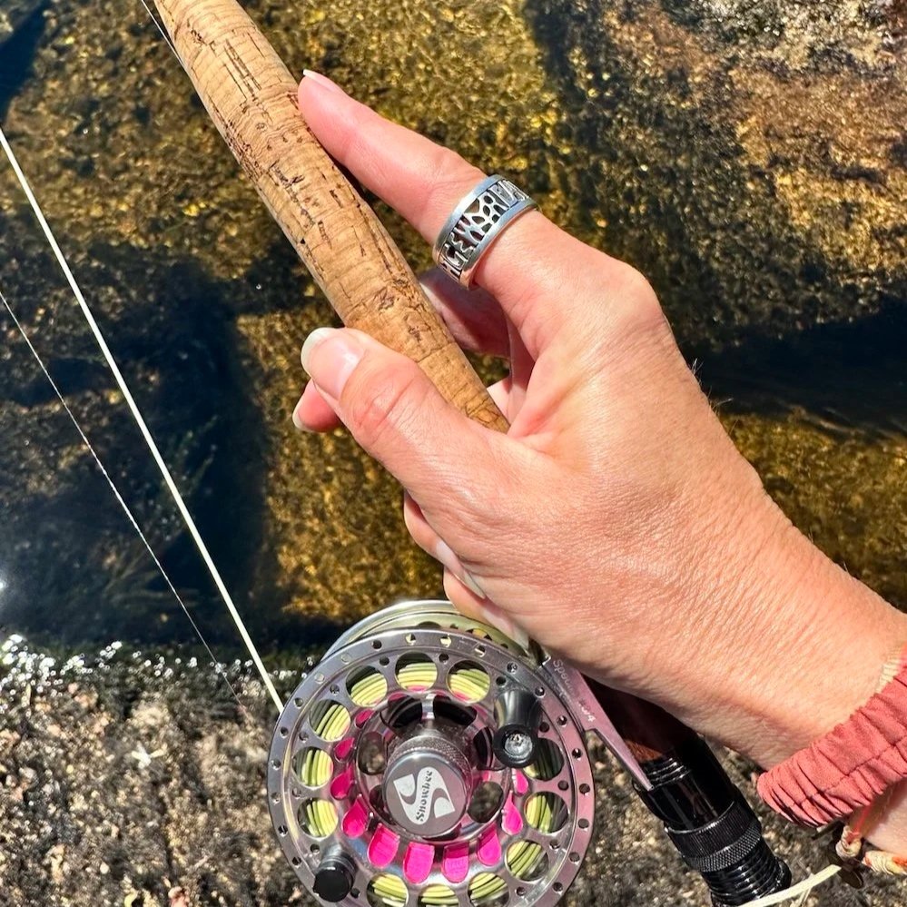 The Alfred Ring, inspired by the words “Aelfred Mec Heht Gewyrcan” from The Alfred Jewel, worn on a woman’s hand holding a fly fishing rod