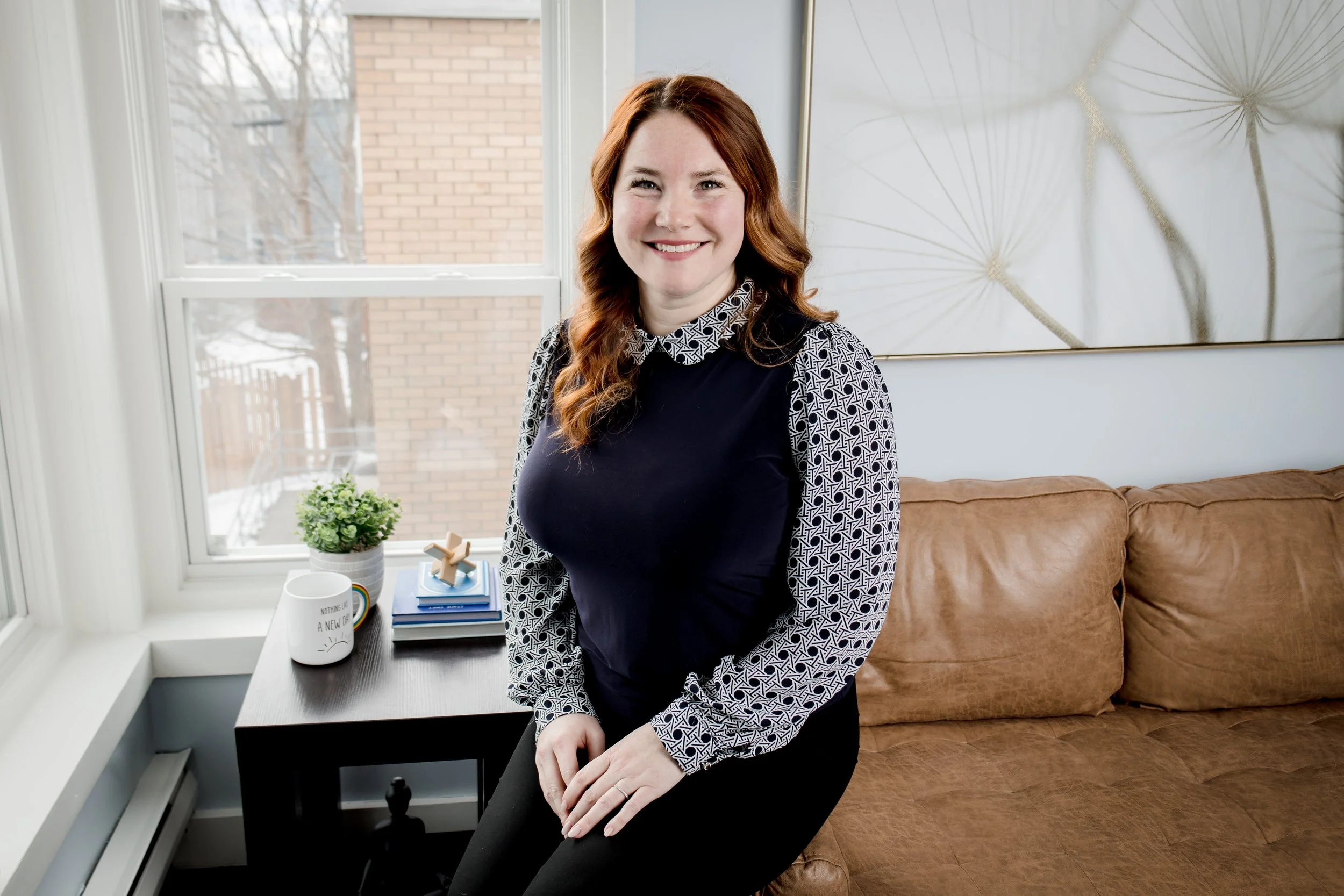 Smiling woman sitting on a beige couch with a patterned top and long red hair.