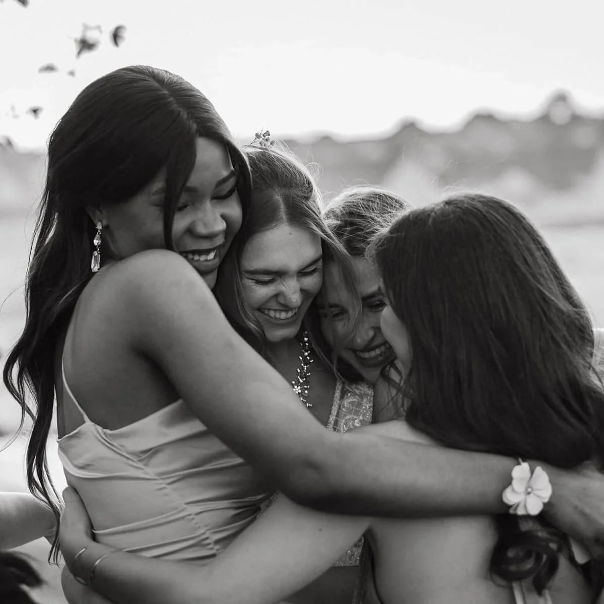 Group of bridesmaids hugging and smiling outdoors. Candid wedding group photo