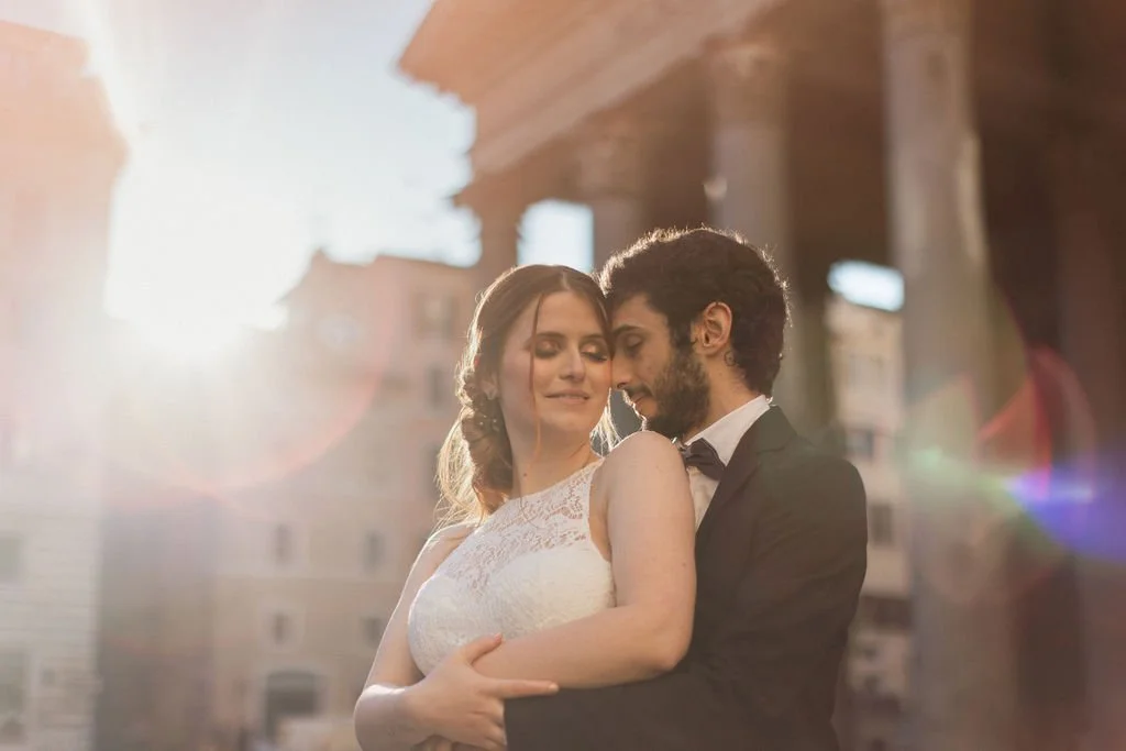 A couple dressed in wedding attire sharing an intimate moment outdoors during sunset.