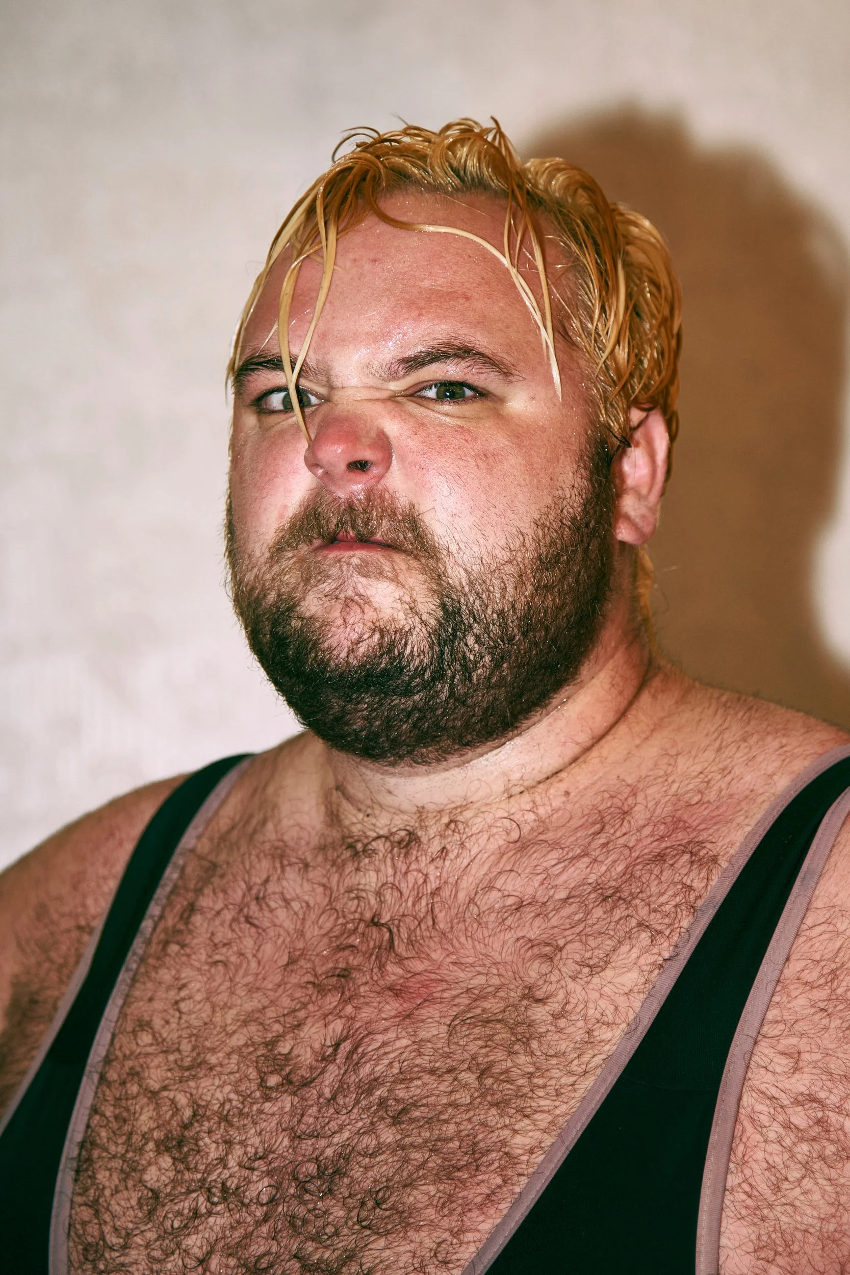 Bearded man with blond hair in a wrestling singlet looking intense.