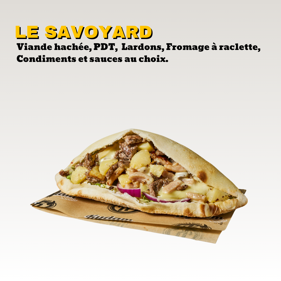 Un sandwich pain maison garnie de viande hachée, pommes de terre, fromage à raclette, oignons, et autres ingrédients, sur un support en papier. Toute notre carte est halal.