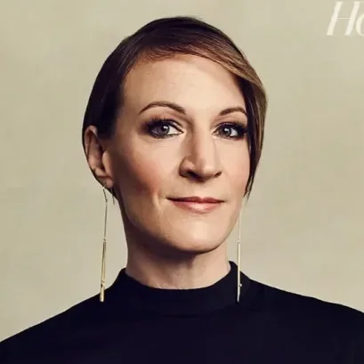 Portrait of a woman with short brown hair, wearing black top and long gold earrings.
