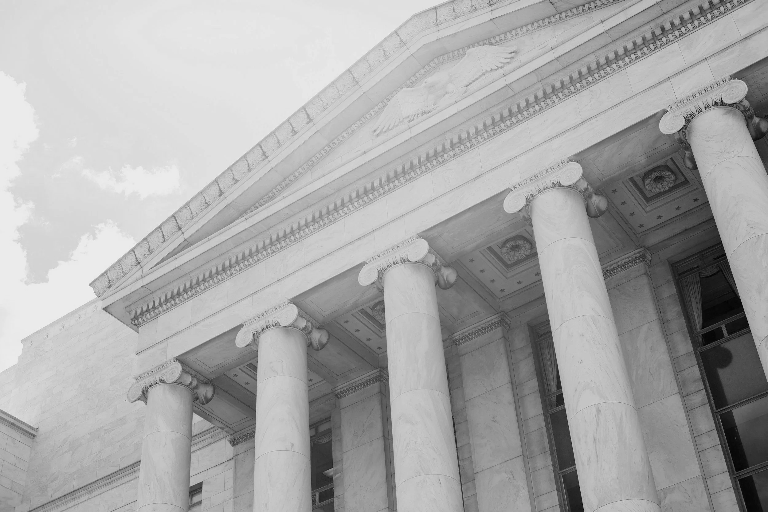 Close-up of a classical building's facade showcasing large columns, detailed architectural designs, and a triangular pediment with a carved figure.