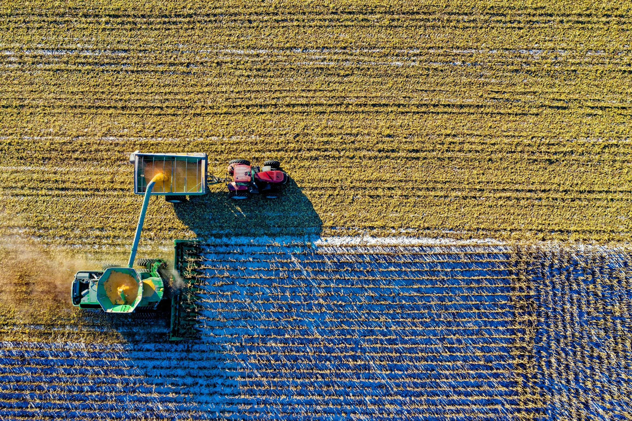 An aerial view of a tractor harvesting crops in a field, with a grain truck attached to collect the harvest.