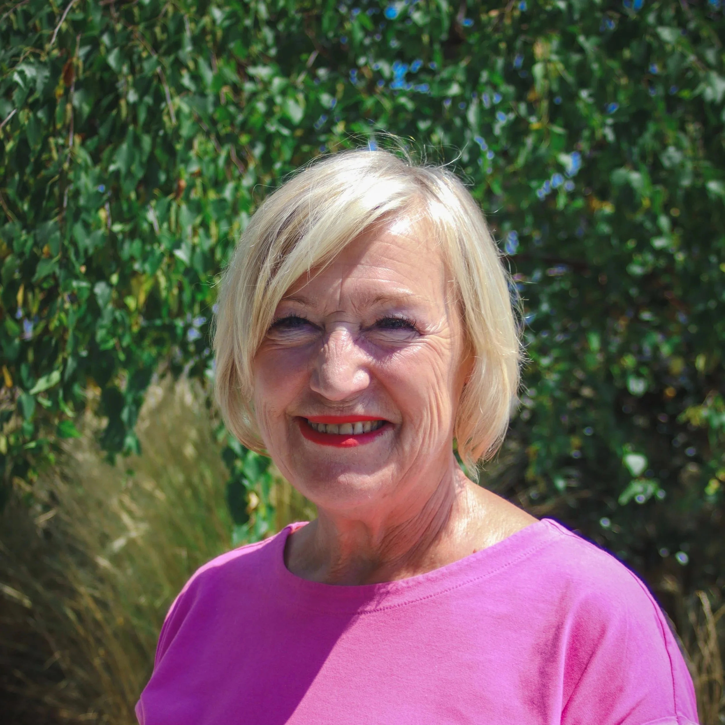 Smiling woman with blond hair standing in front of a brick wall.