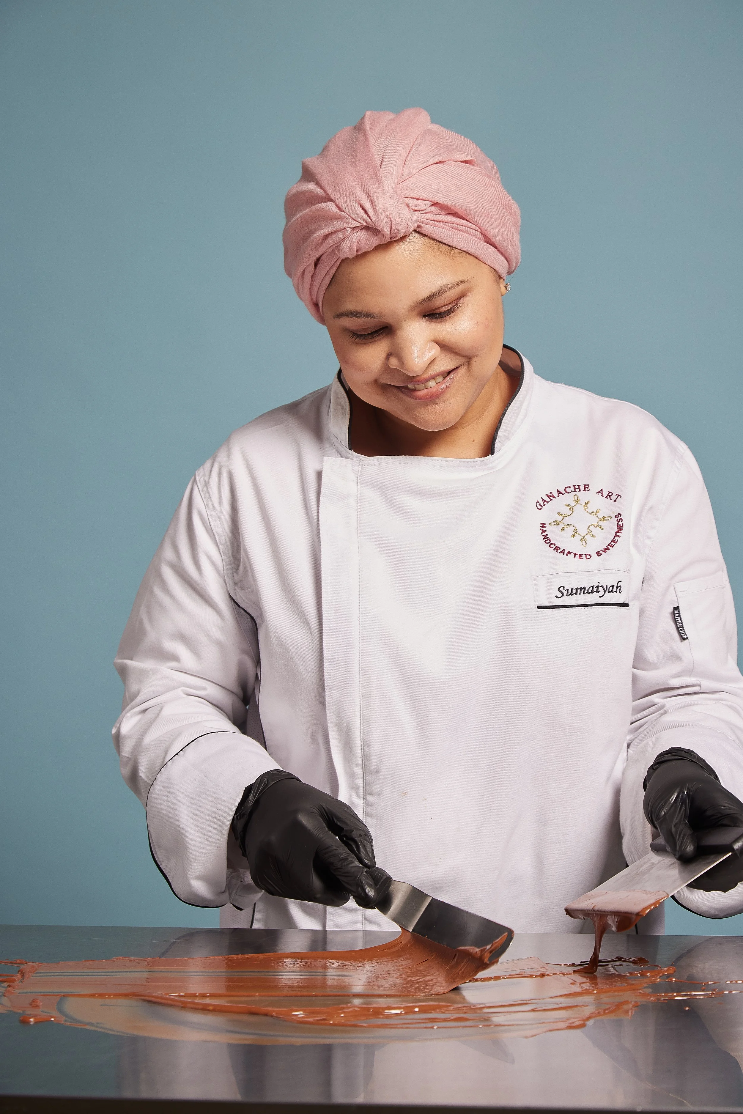 A hand holding a smartphone displaying Arabic text and translation, with a blurred black keyboard, white book, and electronic devices on a black desk in the background.